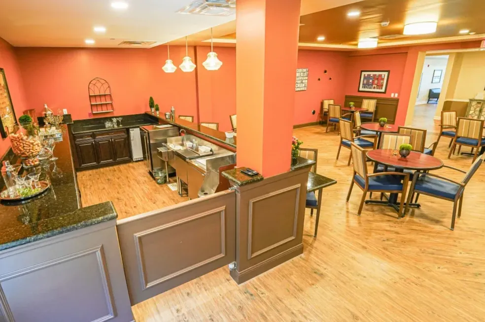 Interior of a dining area with a bar, featuring orange walls, wooden floors, and round tables with blue chairs.