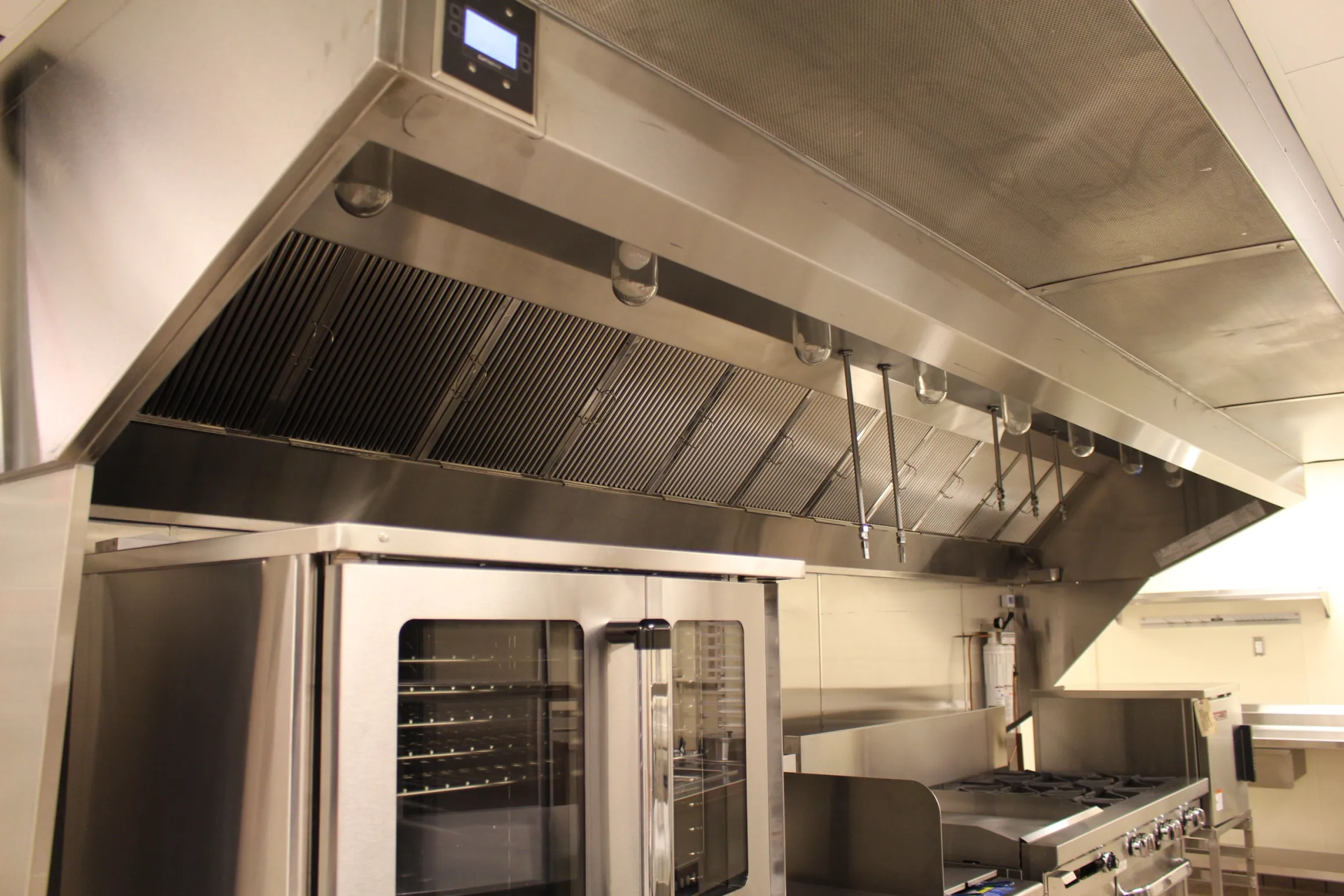 Commercial kitchen hood over a double oven and stovetop. Stainless steel appliances in a restaurant kitchen.