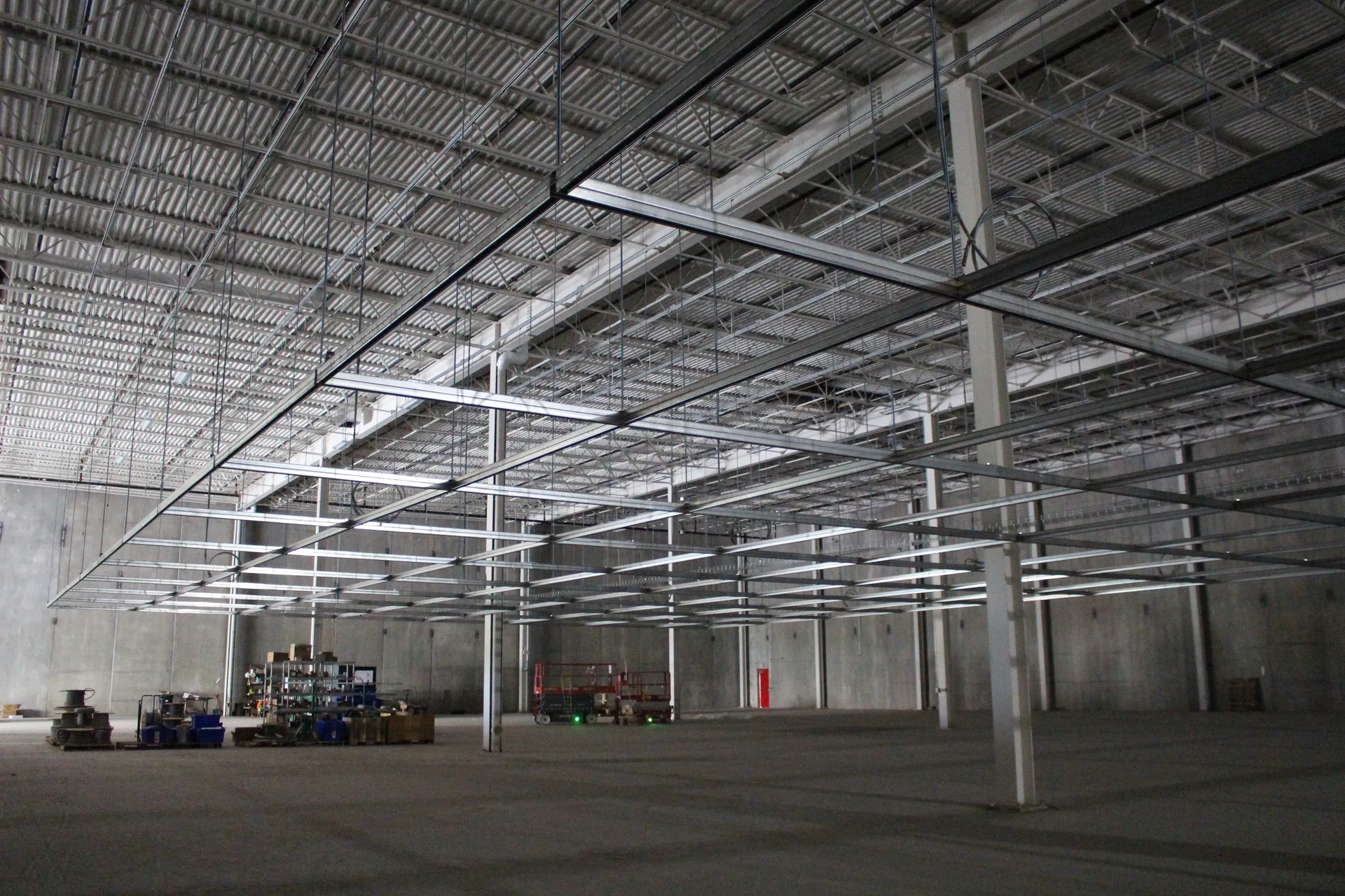 Interior view of a large warehouse with a metal ceiling, supporting beams, and equipment on the floor.