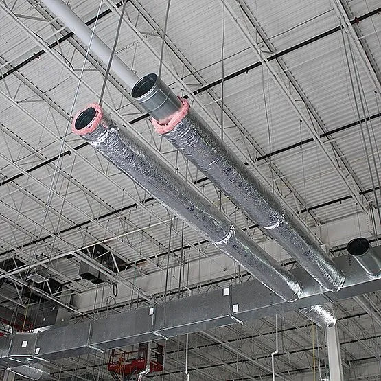 Insulated metallic HVAC ductwork suspended from the ceiling of a large industrial building.