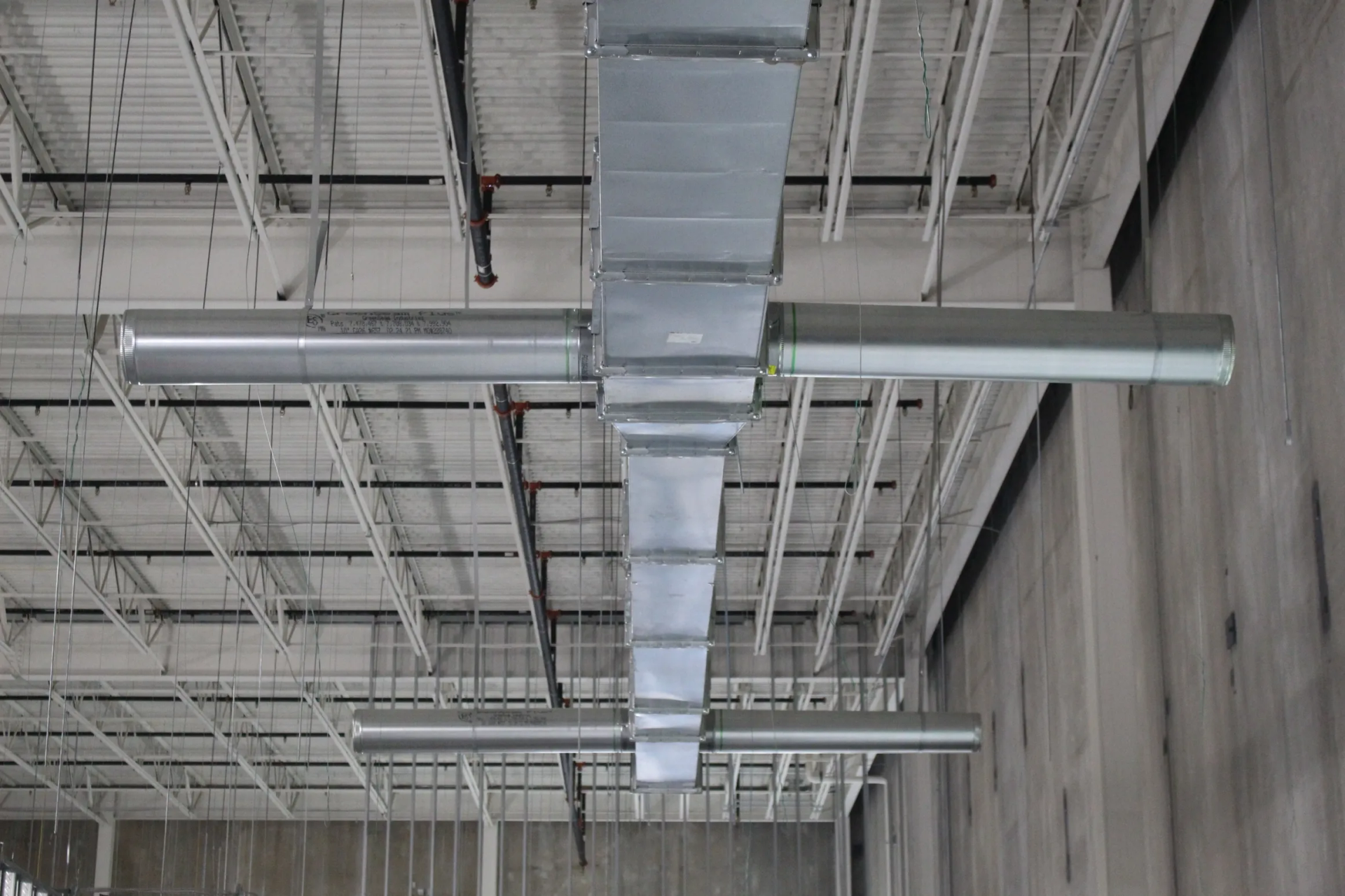 HVAC ductwork suspended from a commercial building ceiling. Rectangular ducts feed into cylindrical air diffusers.