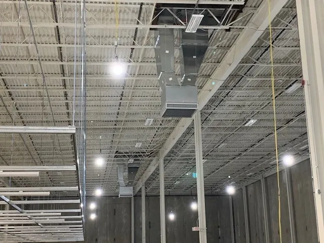 Interior of a building with exposed ceiling, metal ventilation, and lights. Concrete walls are in the background.