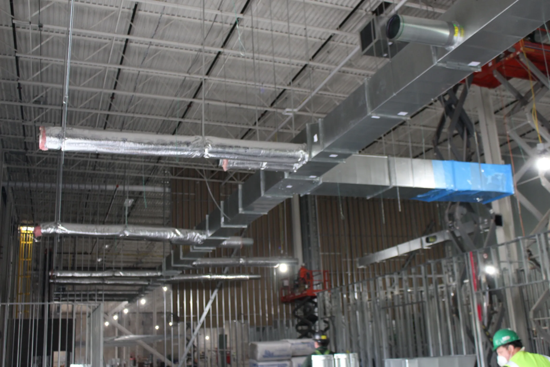 HVAC ductwork installation in a commercial building under construction. Silver ducts, exposed ceiling, studs.