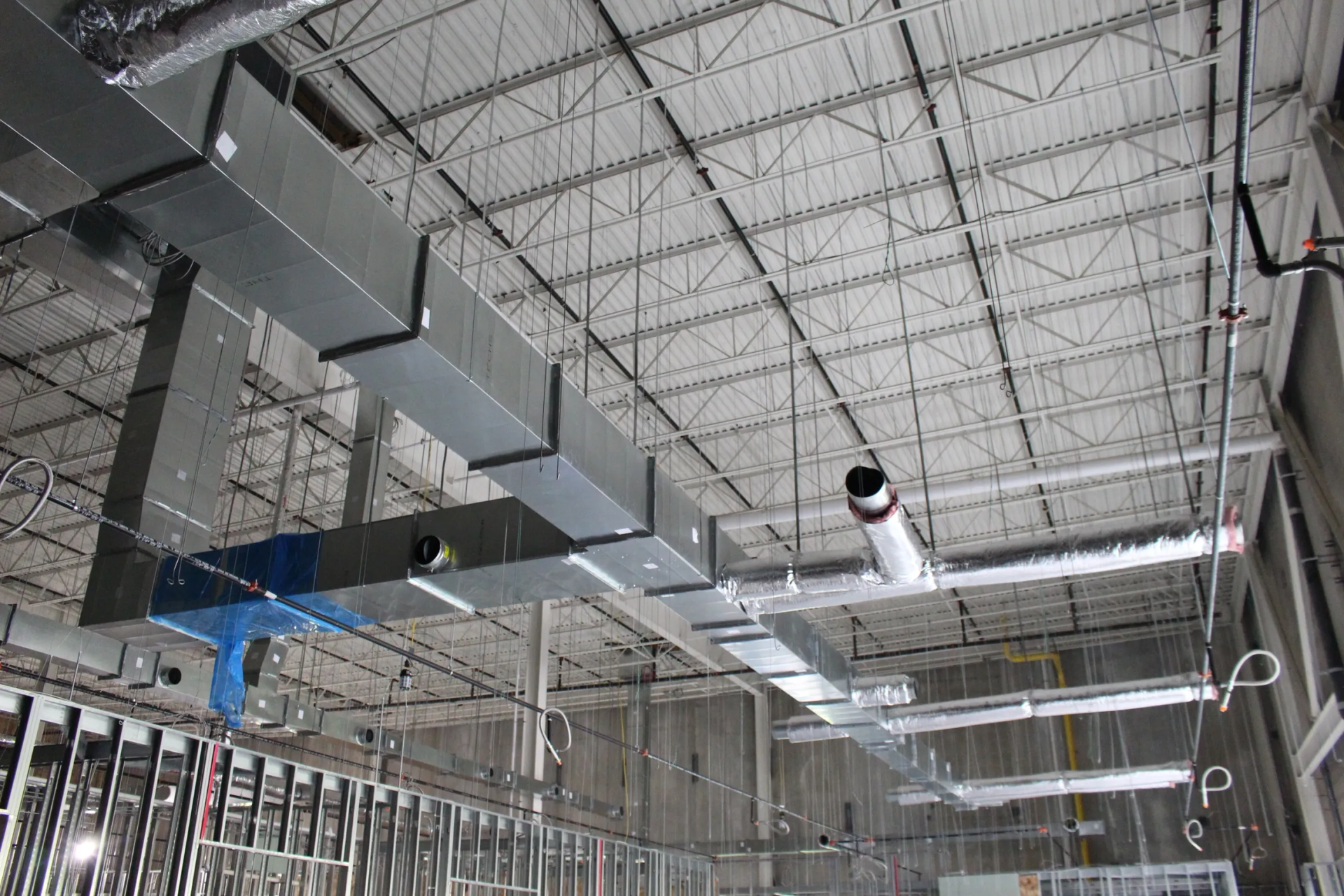 HVAC ductwork installed on a building ceiling with metal framing and a white corrugated roof.