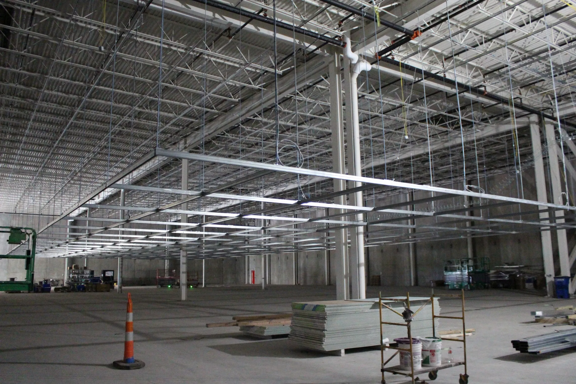 Interior of a large warehouse under construction, showing metal framework, support beams, and unfinished floor.