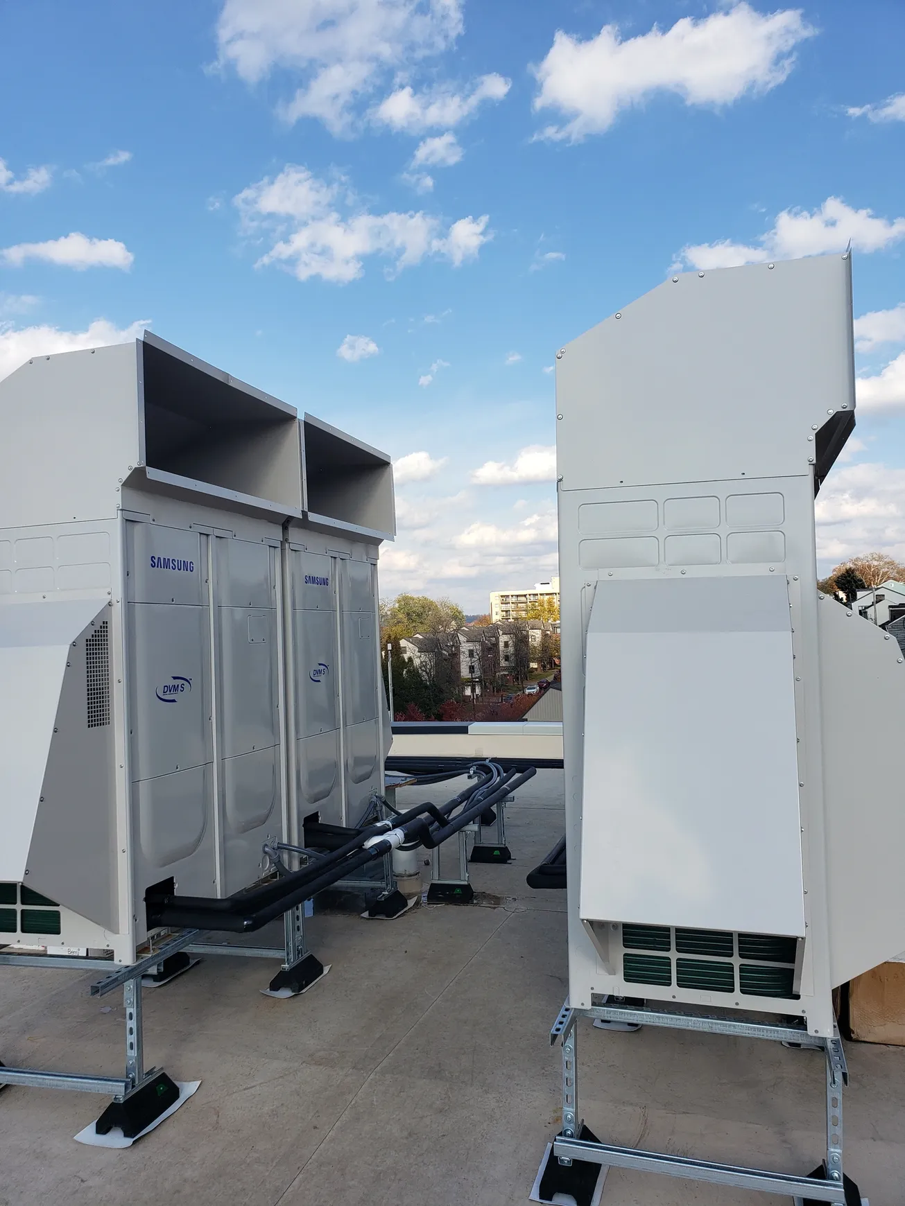 Two large white HVAC units on a rooftop against a blue sky with clouds.