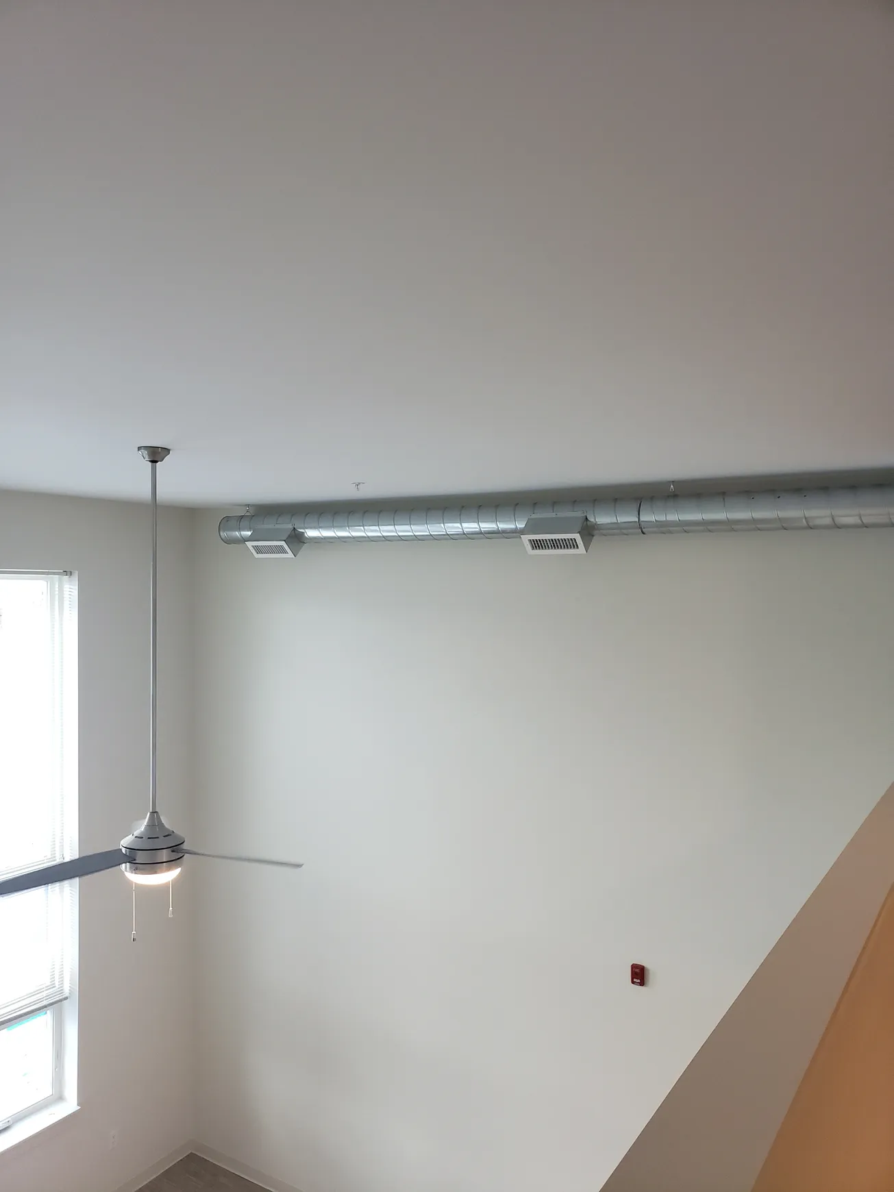 High-ceilinged room with a ceiling fan, HVAC ductwork, and a window.