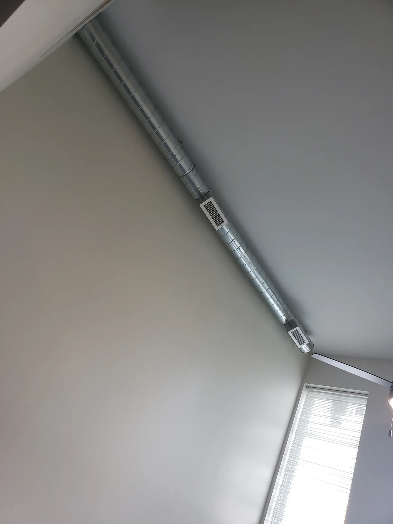 Metal support beam angled across a ceiling, near a window with blinds.
