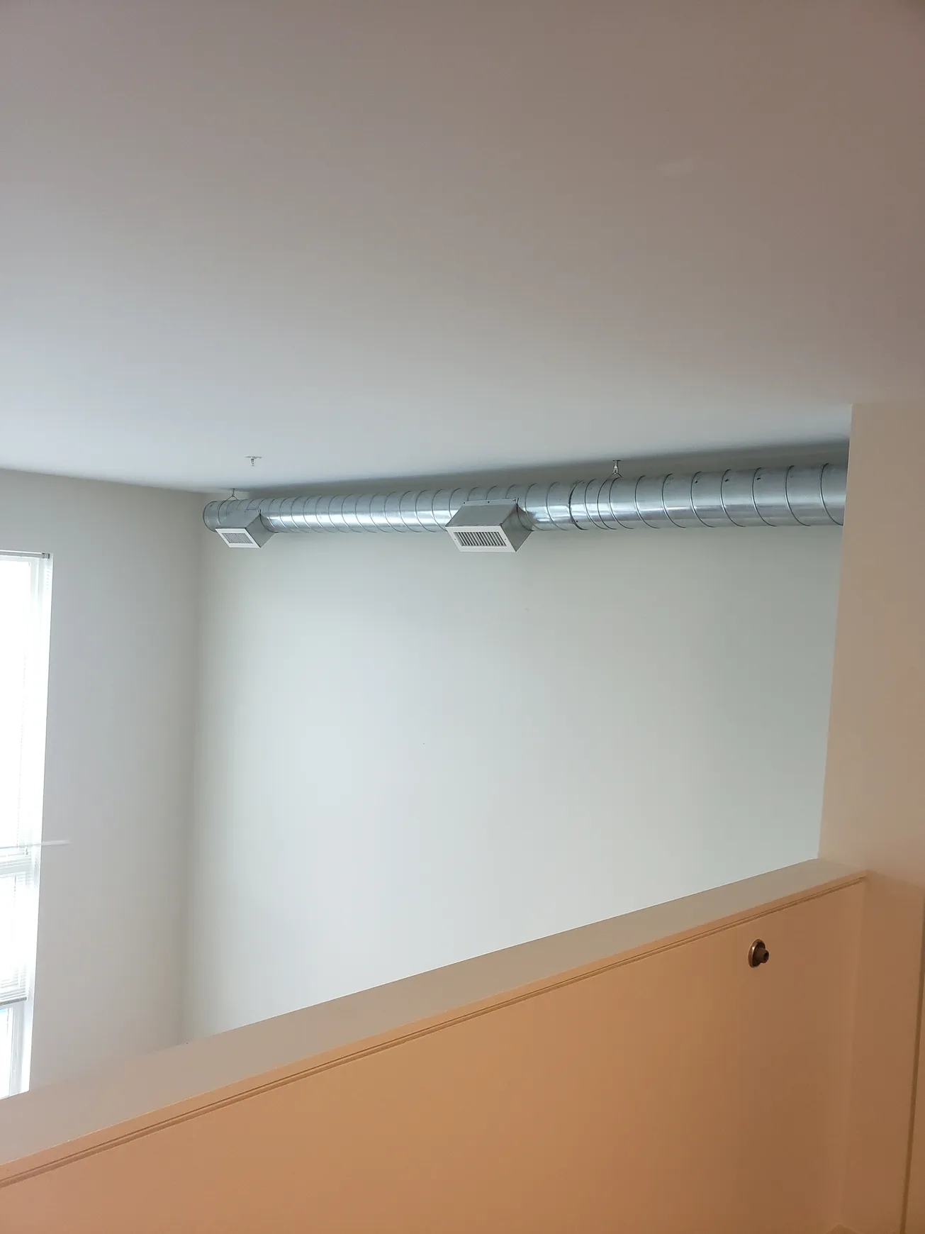 Interior view of a white room with a metal ventilation duct running horizontally near the ceiling.