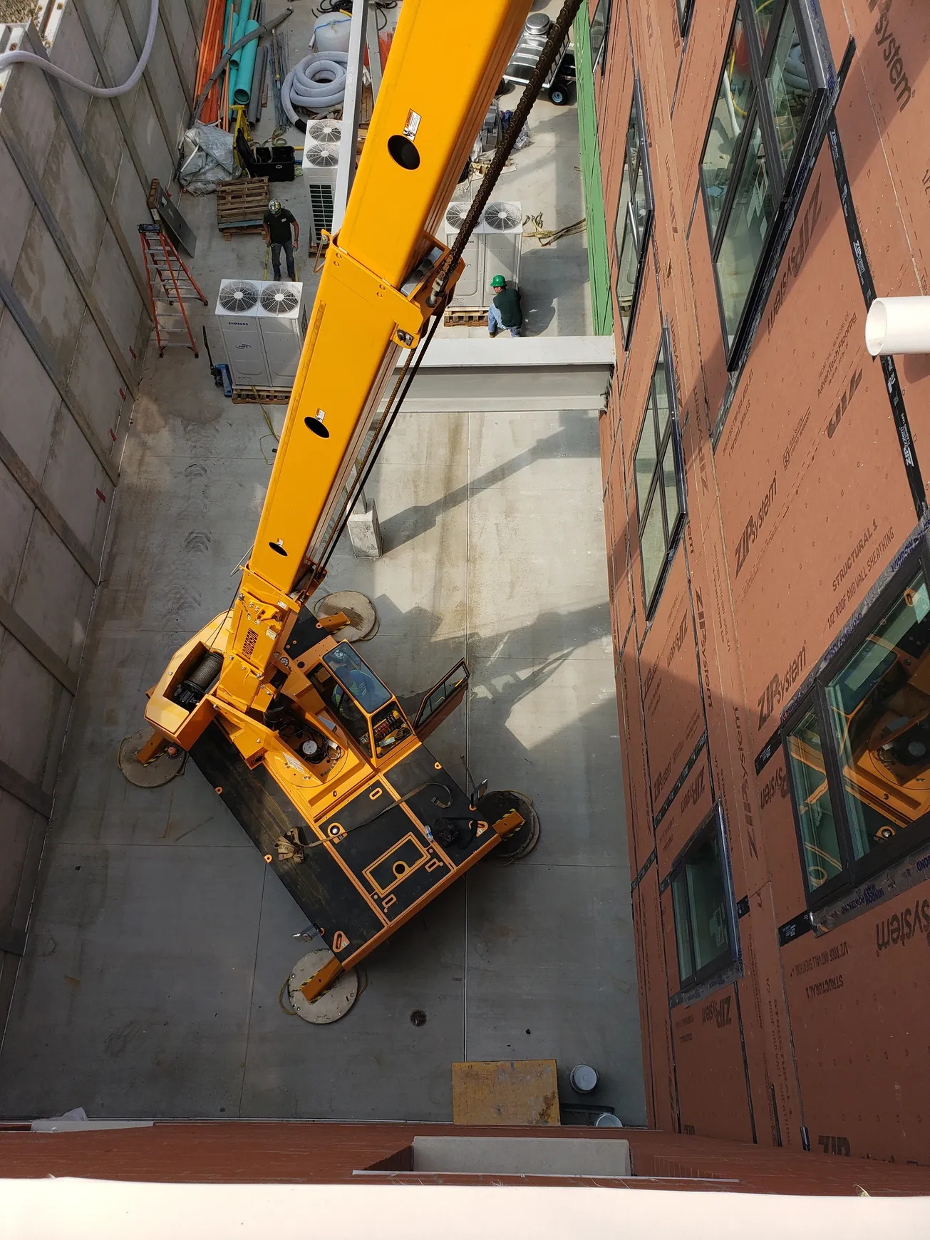 A yellow construction crane arm positioned against a building with windows, operating in a tight space.