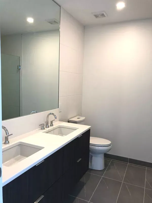 Modern bathroom with a double sink vanity, toilet, and large mirror. Gray tiled floor and white walls.