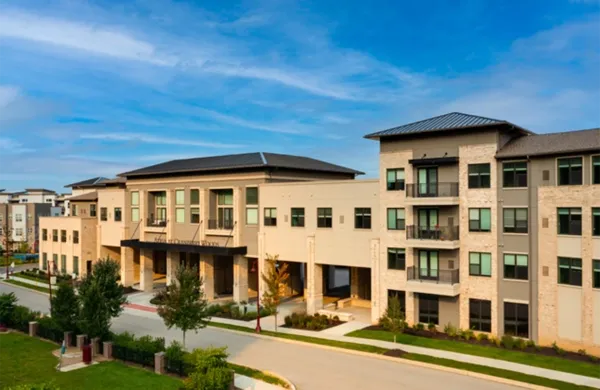 Multi-story apartment building with tan stucco exterior under a blue sky.