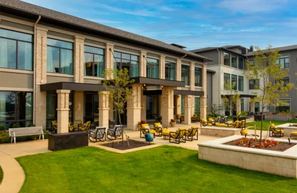 Exterior of a modern building with a covered patio area, featuring outdoor seating and landscaping on a sunny day.