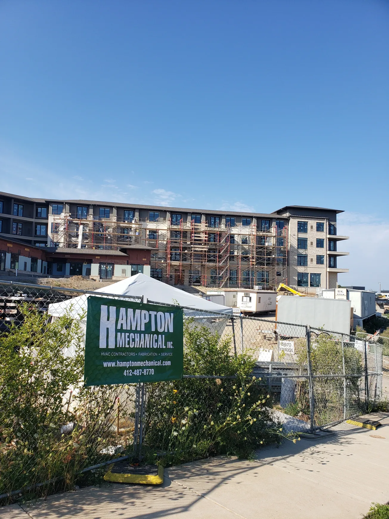 Construction site with a partially built multi-story building. Hampton Utilities Inc. sign in foreground.