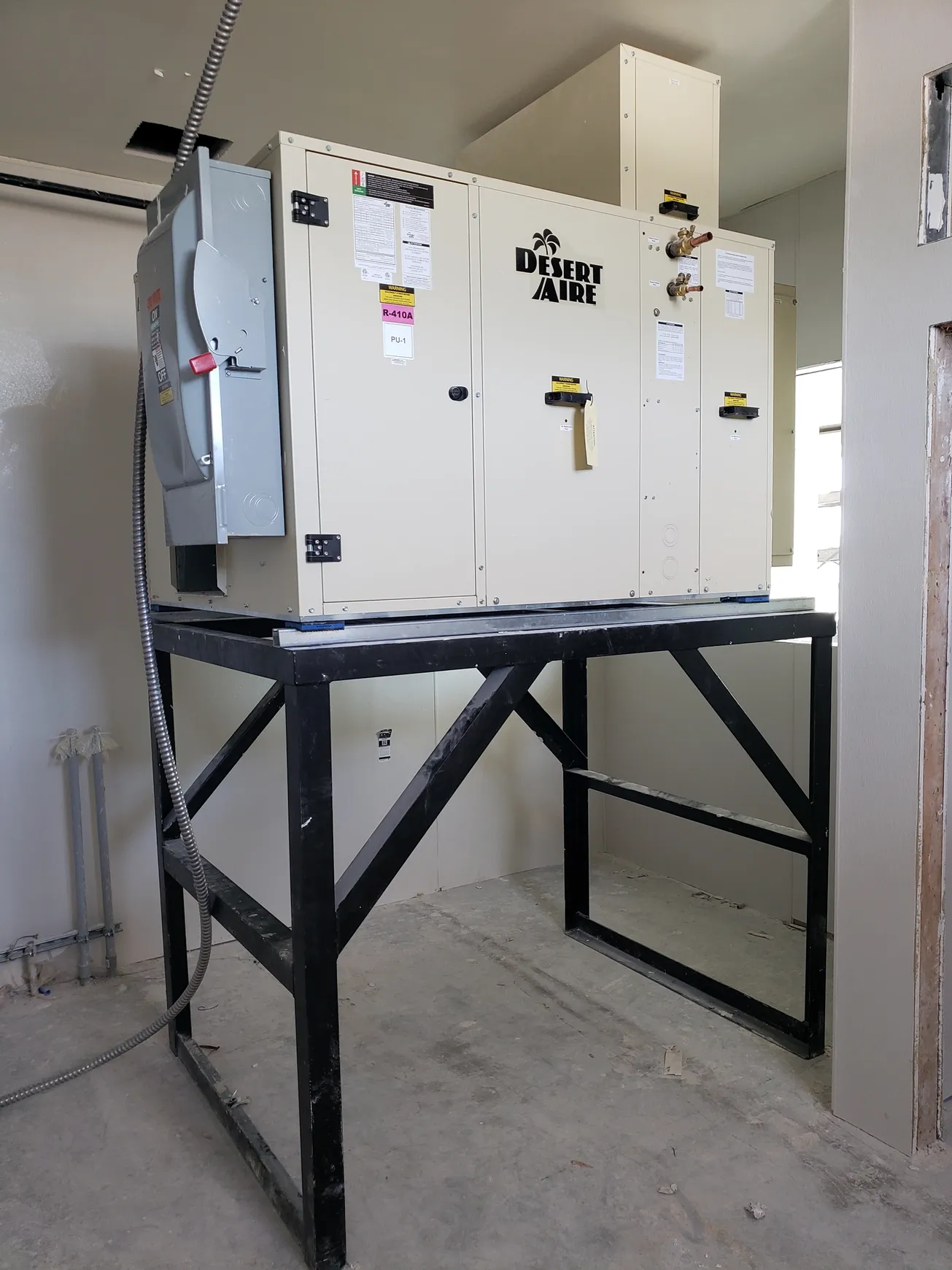 HVAC unit on a black metal platform inside a building under construction, beige and grey.