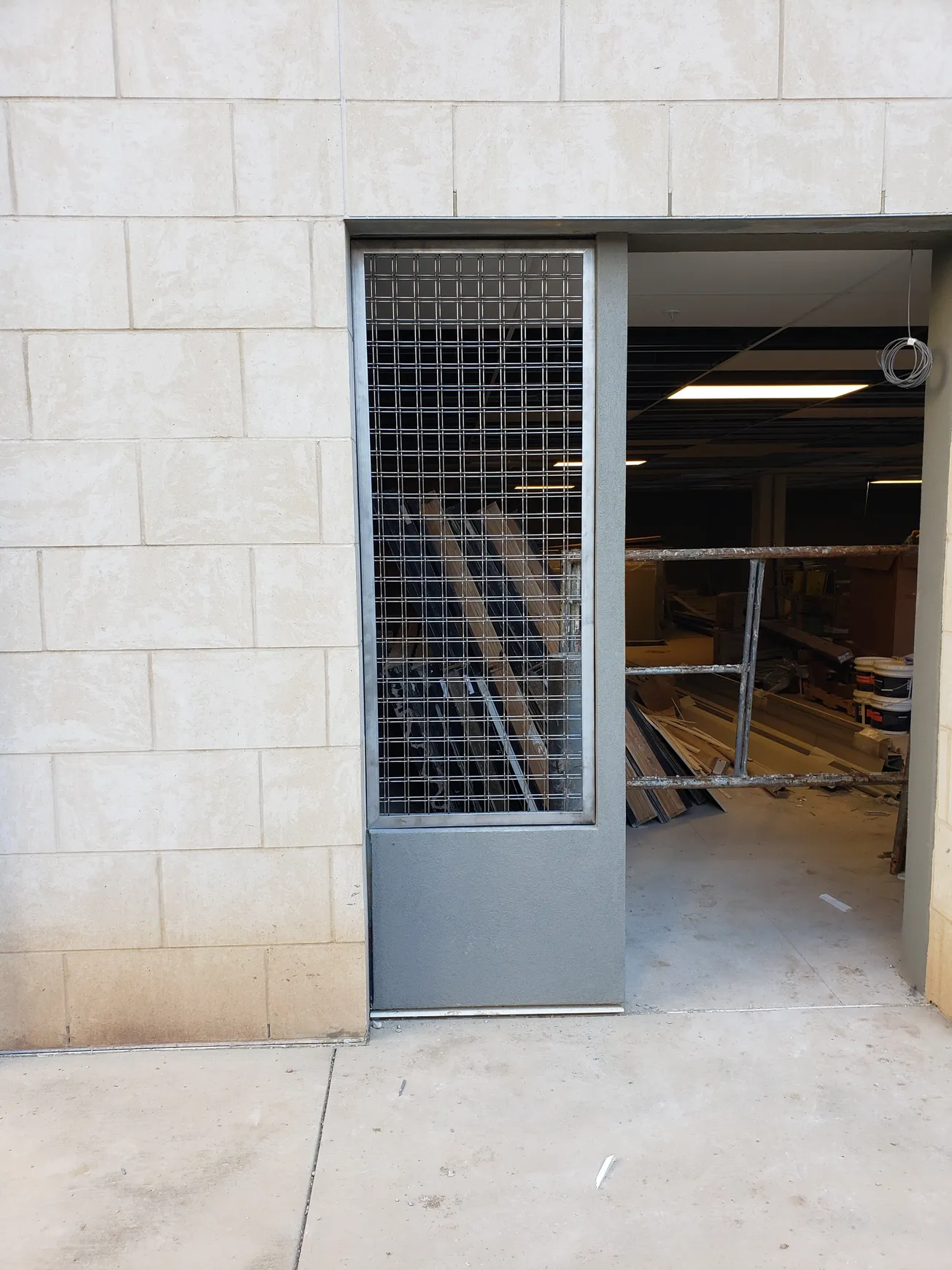 Metal security door in a brick-walled doorway, revealing the interior of a warehouse.