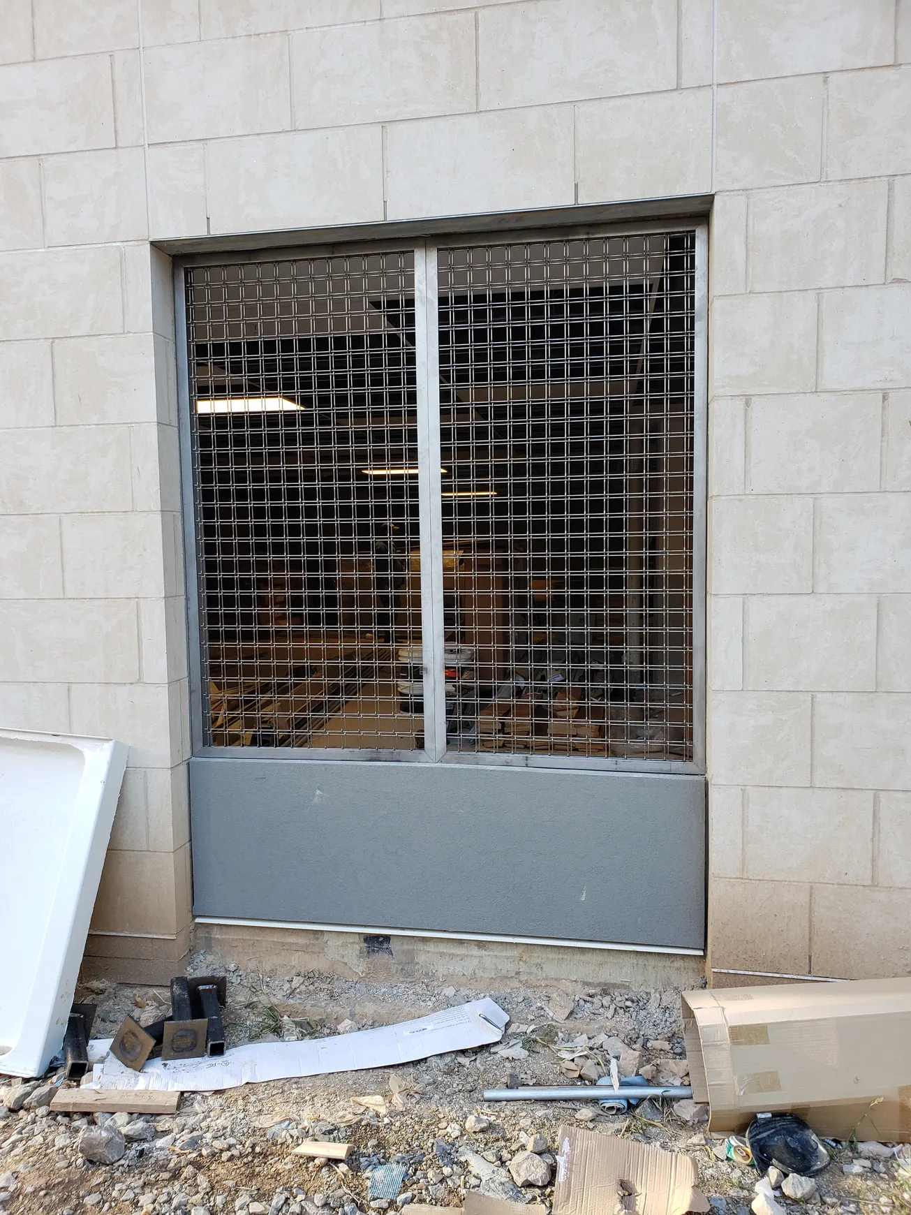 Window with metal security grille, installed in a building with stone block facade.