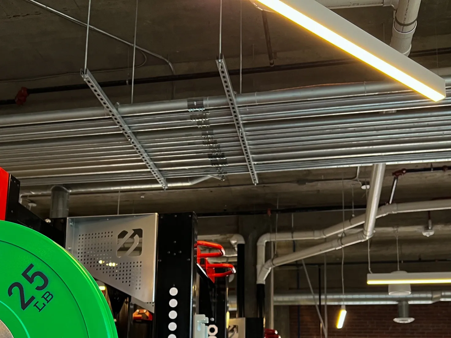 Gym ceiling with electrical conduits, lighting, and a weight plate rack.