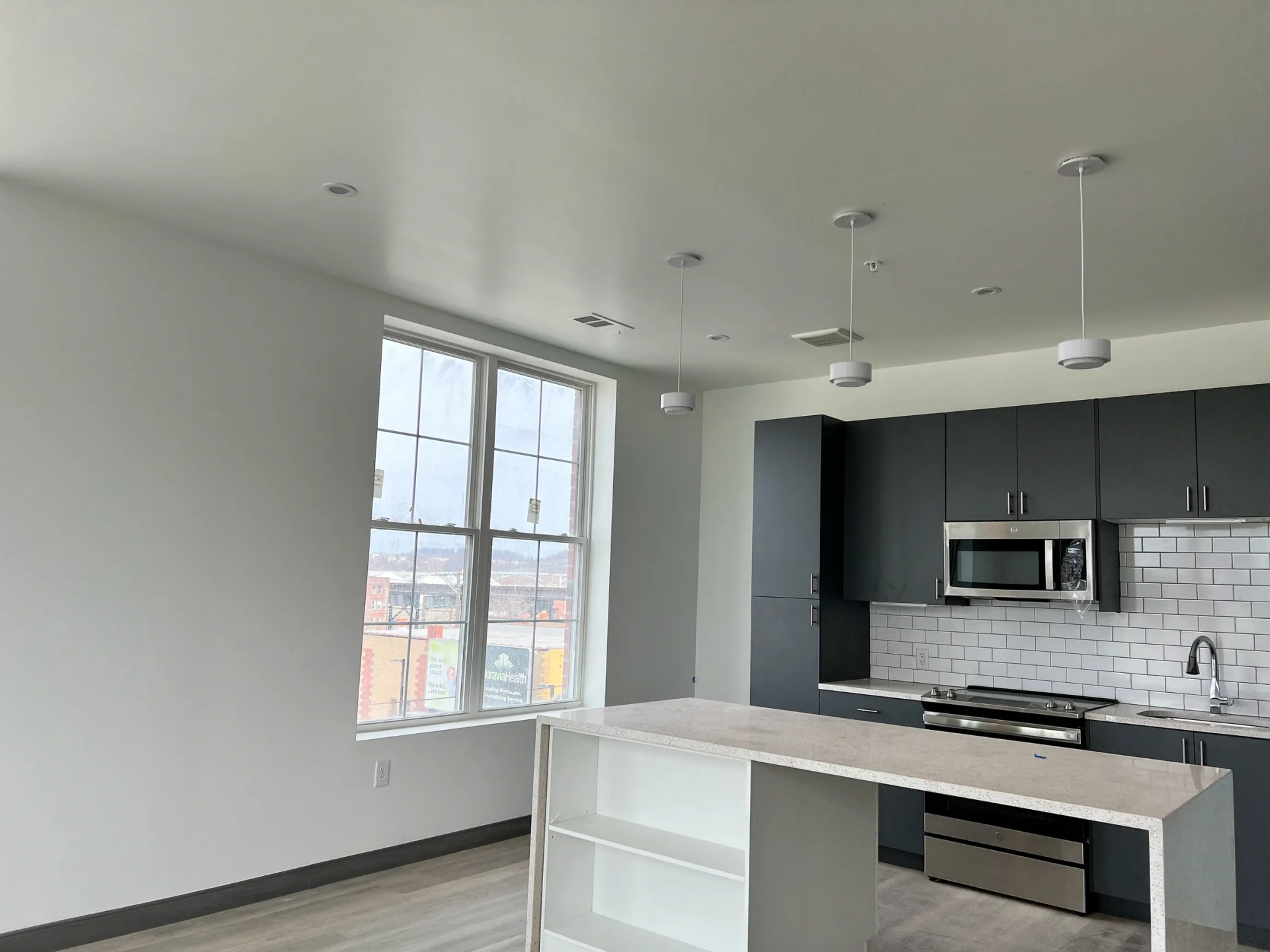 Modern kitchen with dark gray cabinets, white countertops, and three pendant lights.