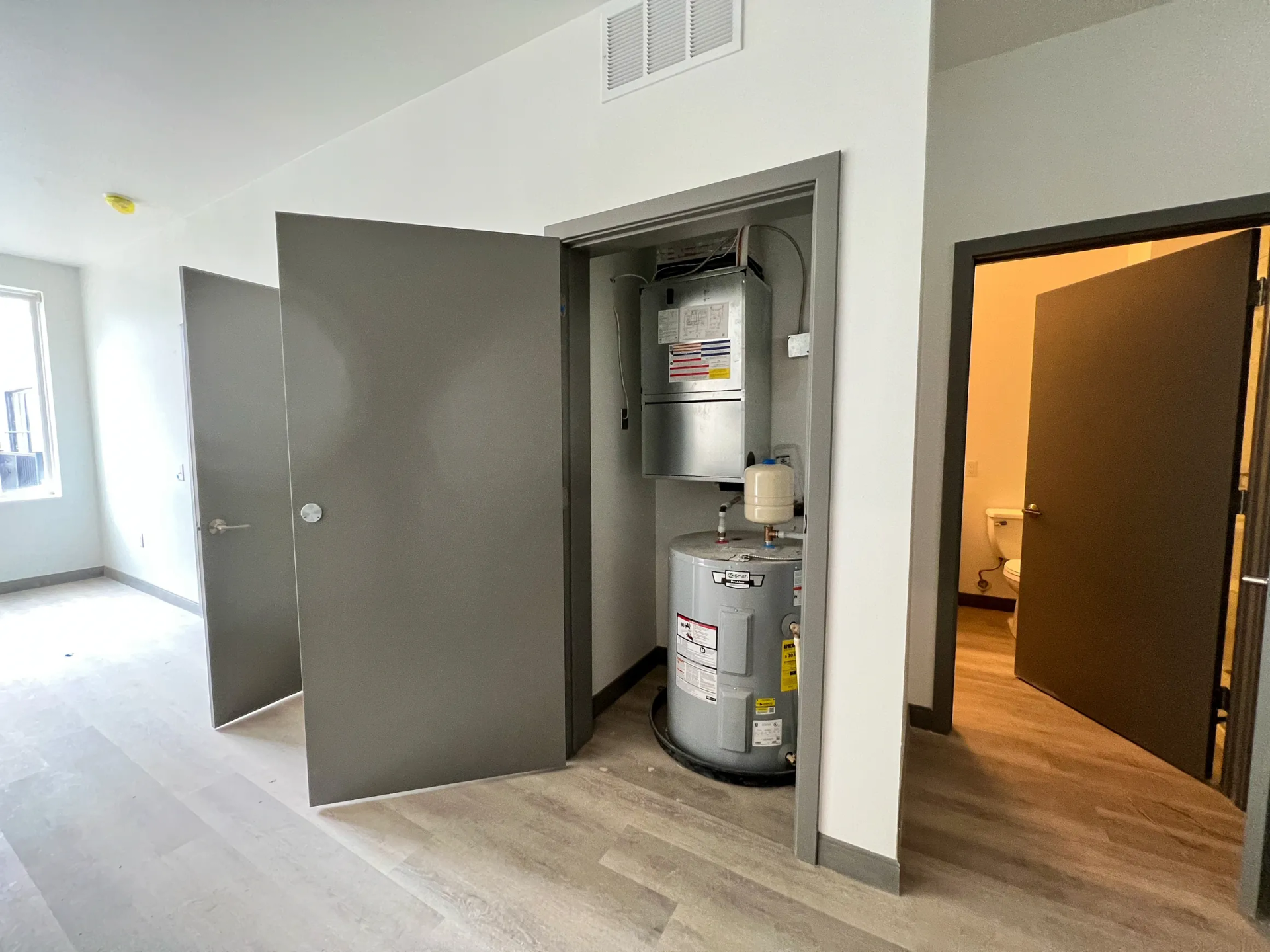 Interior room with open closet housing a water heater and HVAC unit; doors and wood floor.