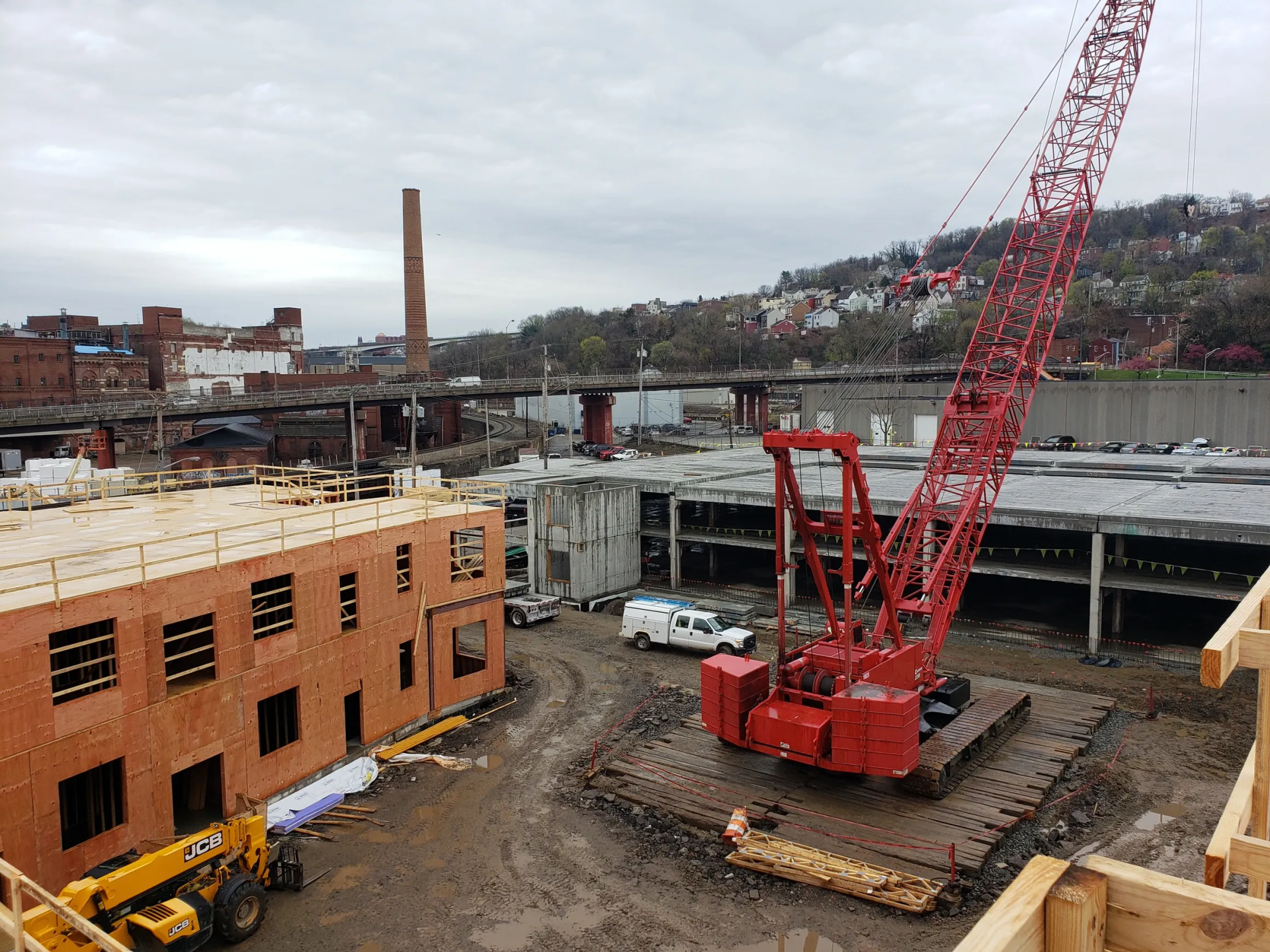 Construction site with red crane, unfinished buildings, and industrial surroundings under a cloudy sky.