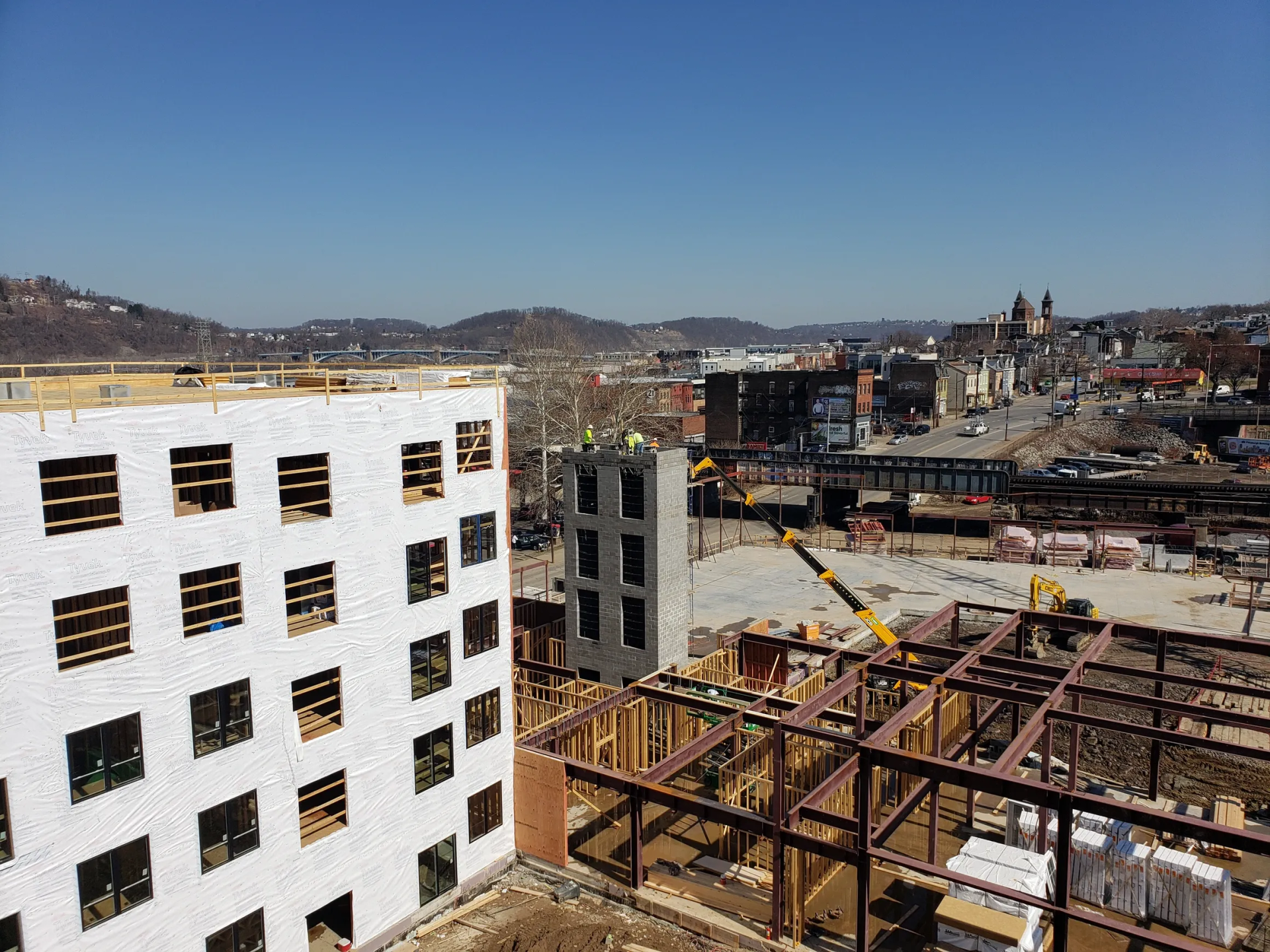 Construction site with several buildings under construction. A crane is visible. Distant hills.