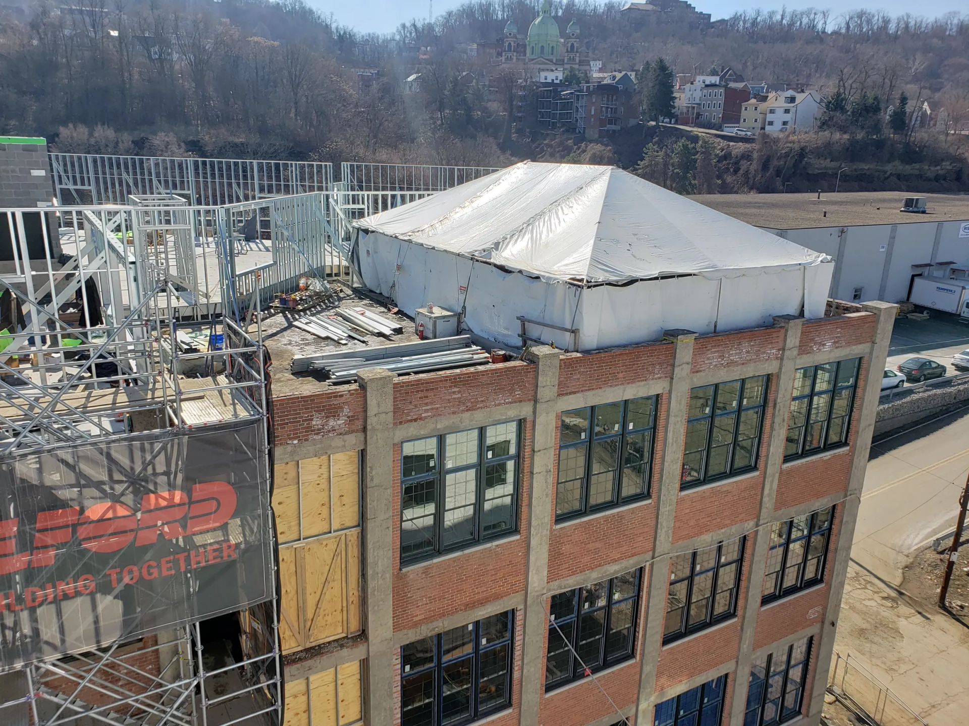 Construction site with a partially built brick building, scaffolding, and a white tent on the roof.