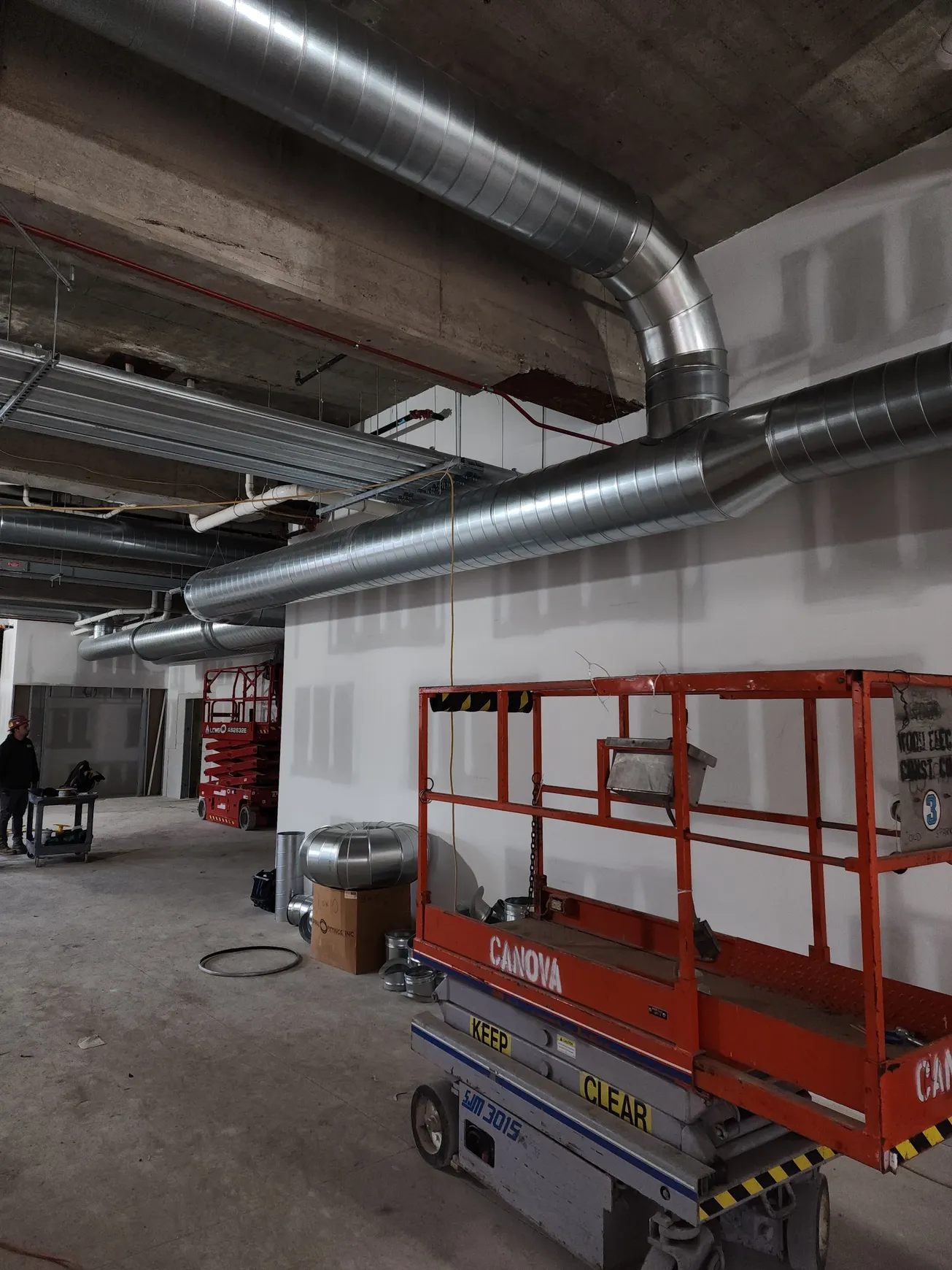 Construction site with ventilation ducts and a red scissor lift.