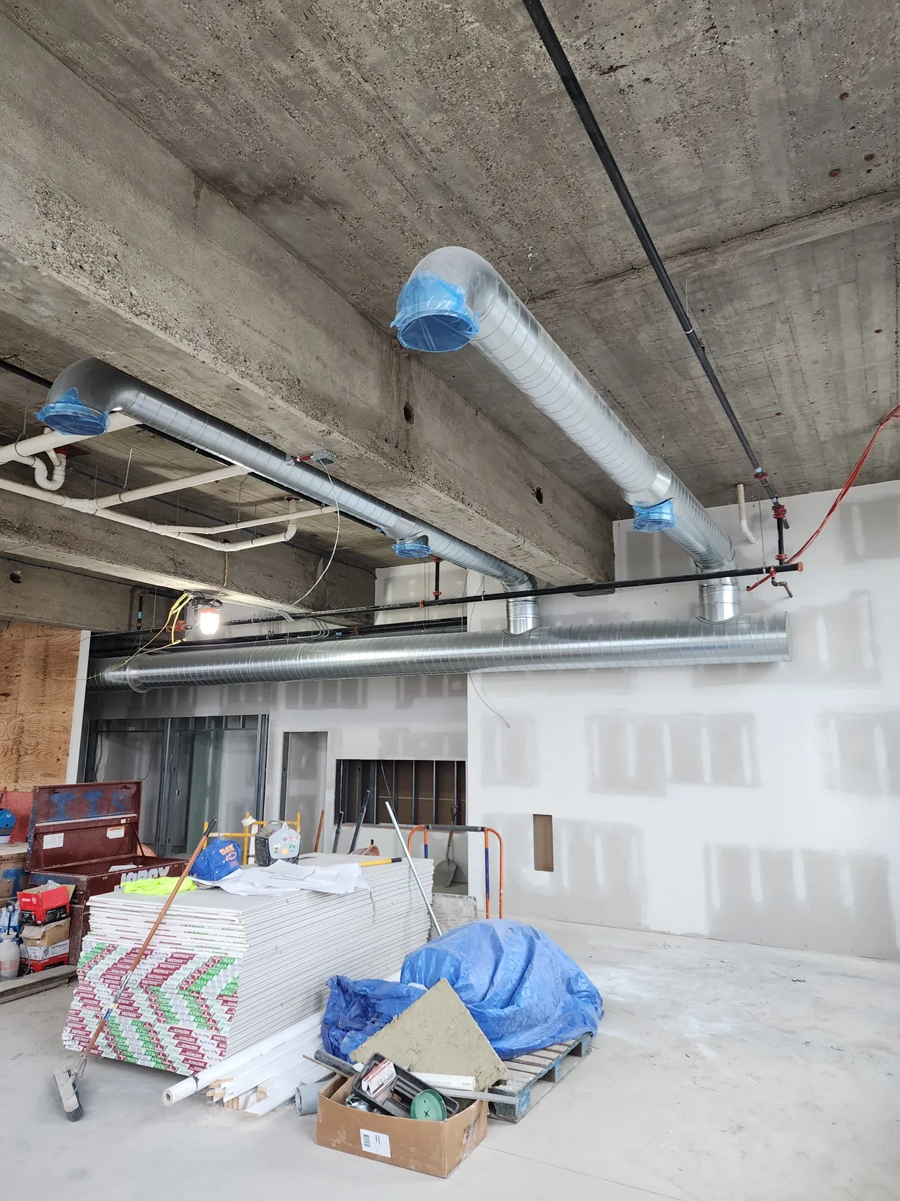 Construction site with exposed concrete ceiling and HVAC ductwork installed.