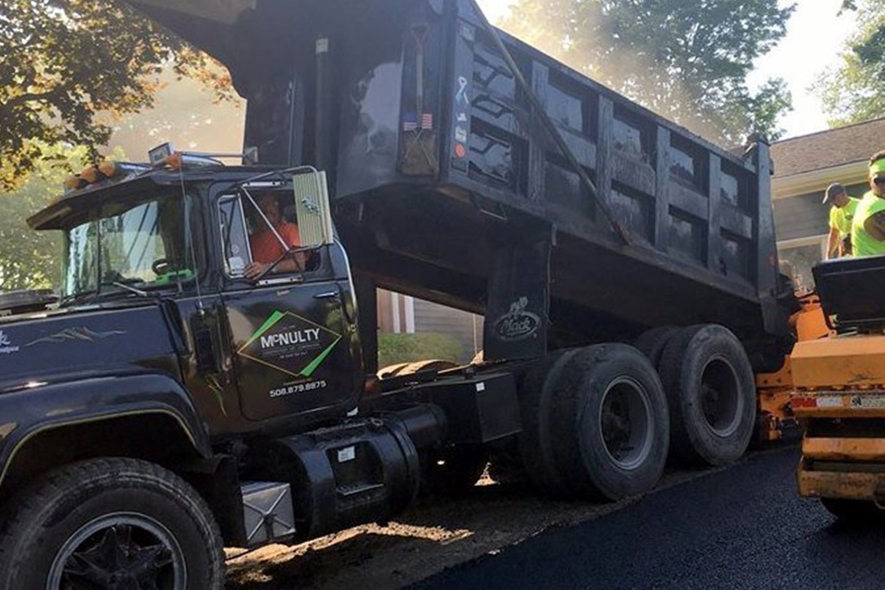 A dump truck is being loaded with asphalt on a road.