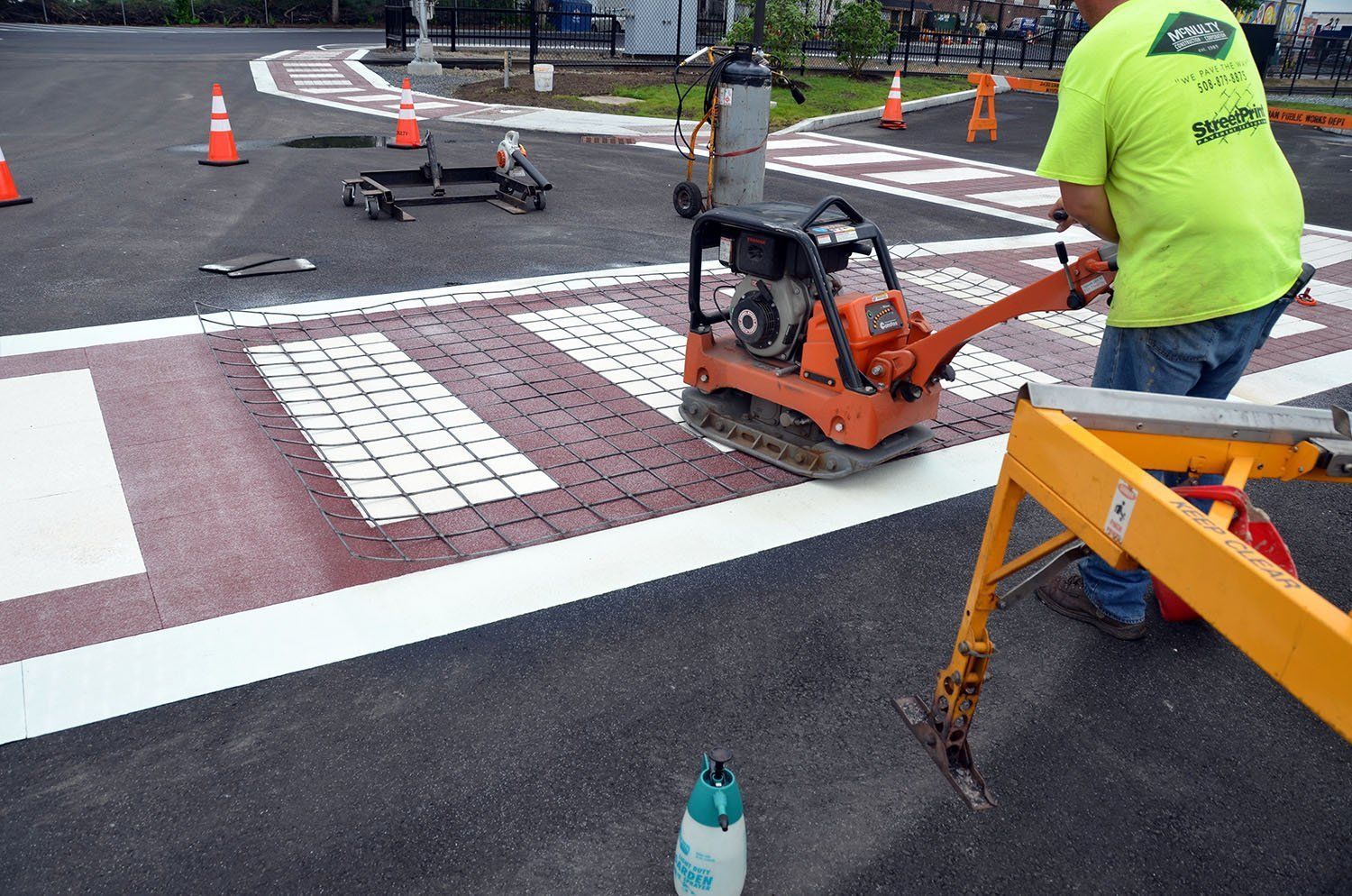 A man in a green shirt is using a machine to paint a crosswalk.