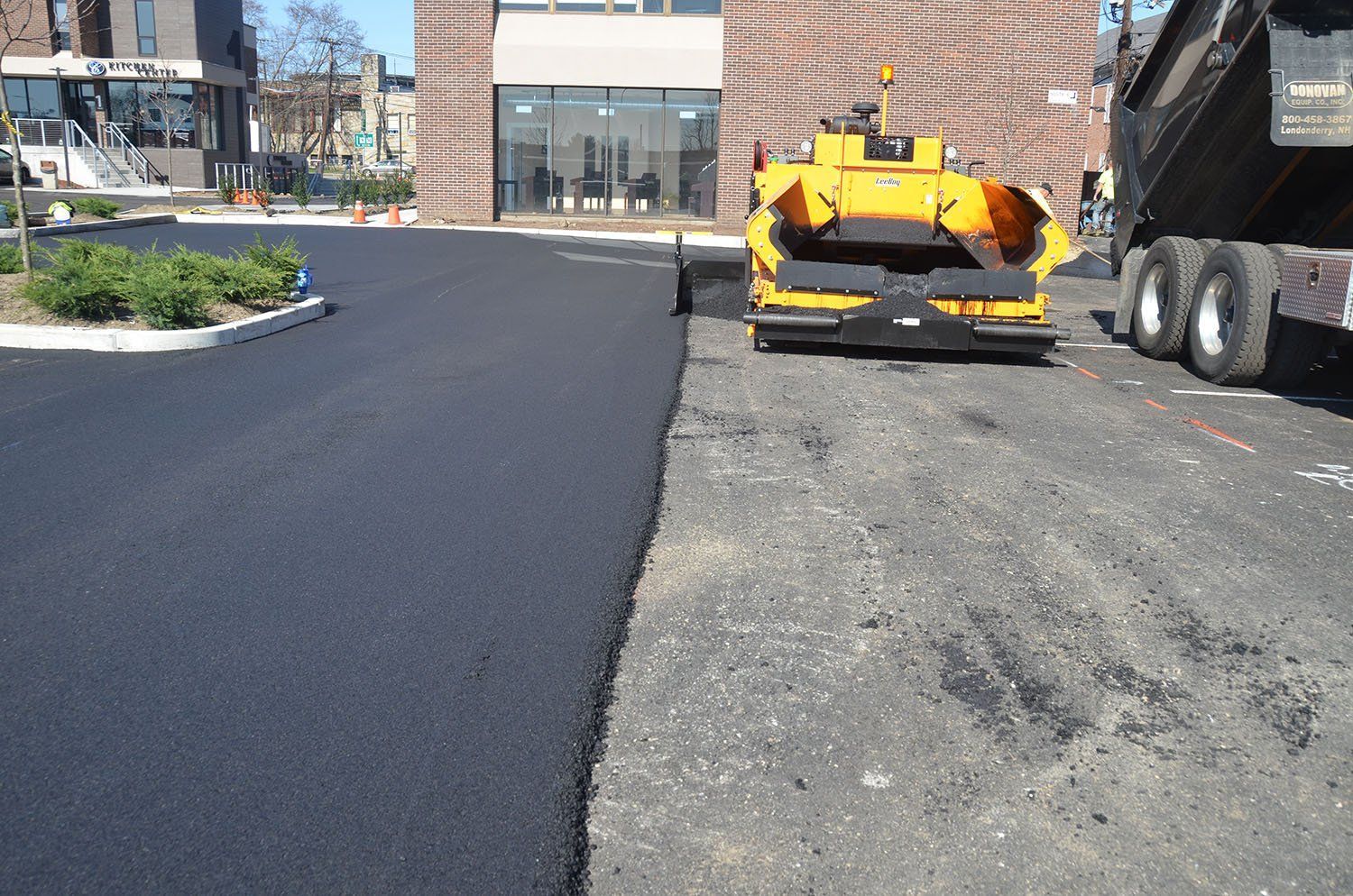 A yellow machine is laying asphalt in a parking lot