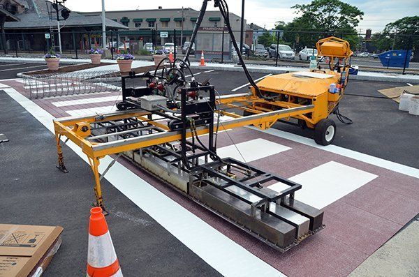 A yellow machine is being used to paint a crosswalk