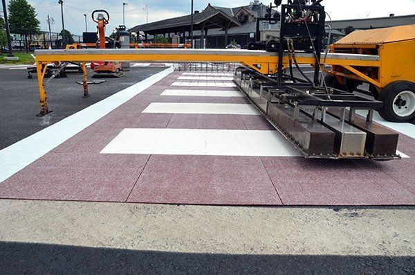 A machine is being used to paint a crosswalk in a parking lot