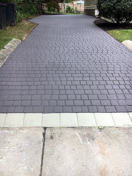 A brick driveway with a white border is leading to a house.