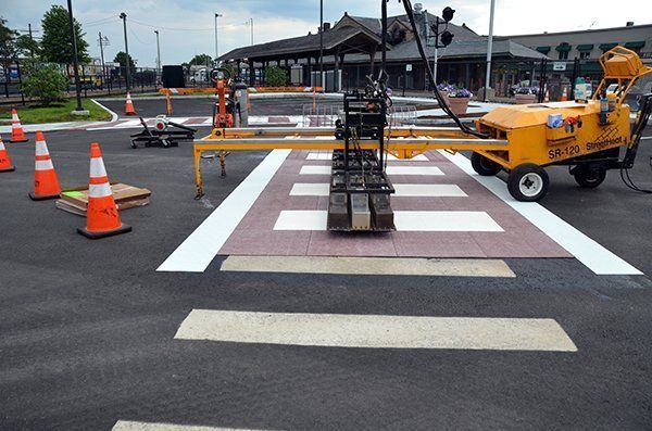 A yellow machine is being used to paint a crosswalk