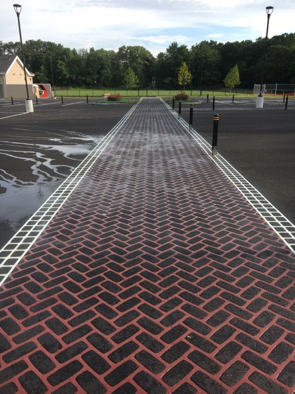 A brick walkway in a parking lot with trees in the background