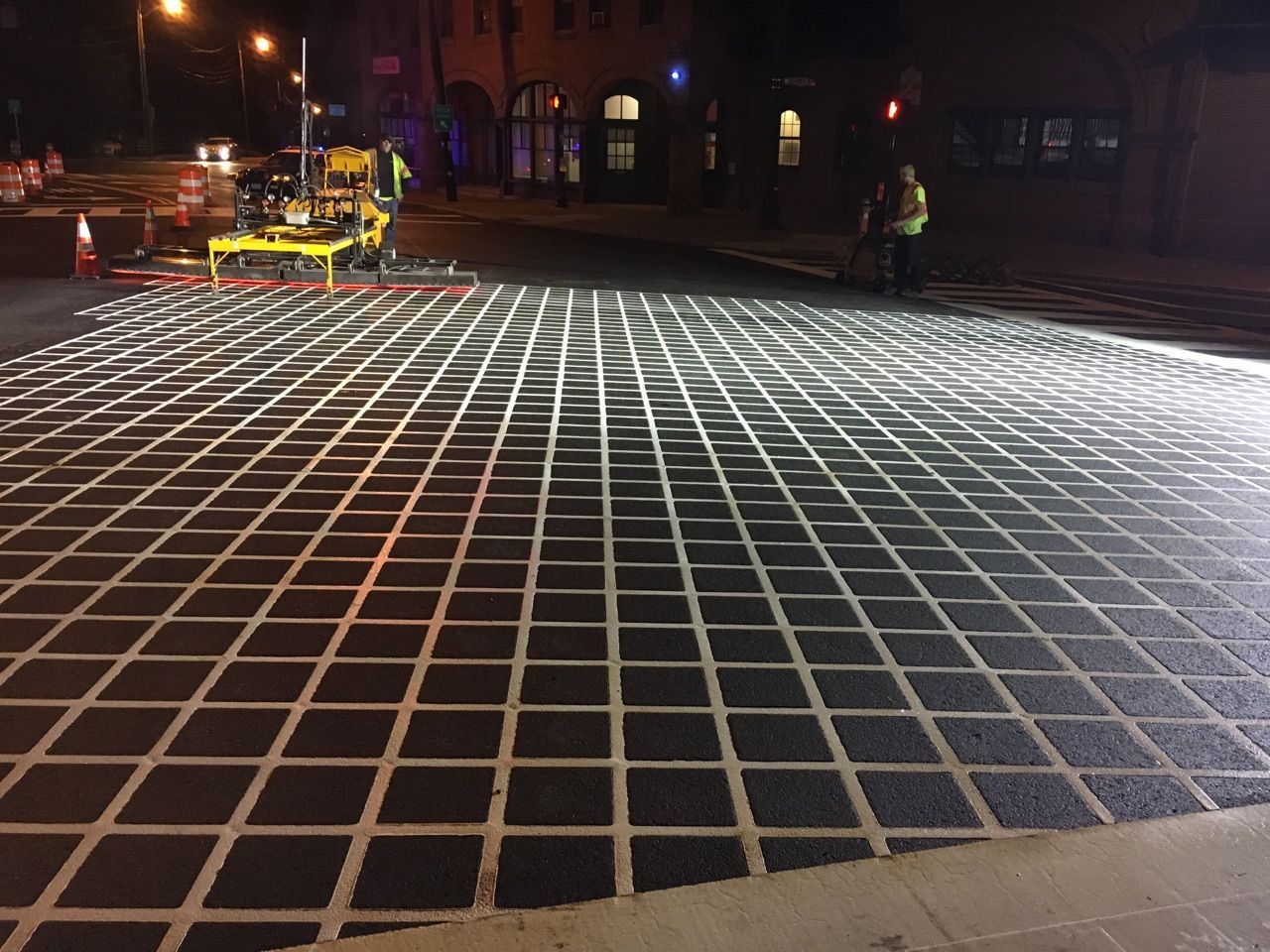 A grid pattern is being painted on a street at night