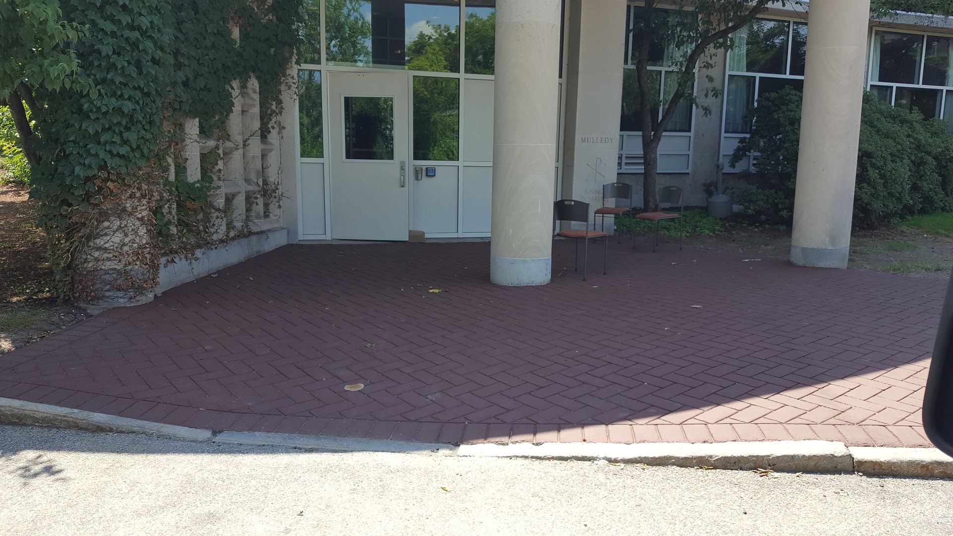 A car is parked in front of a building with a brick driveway.