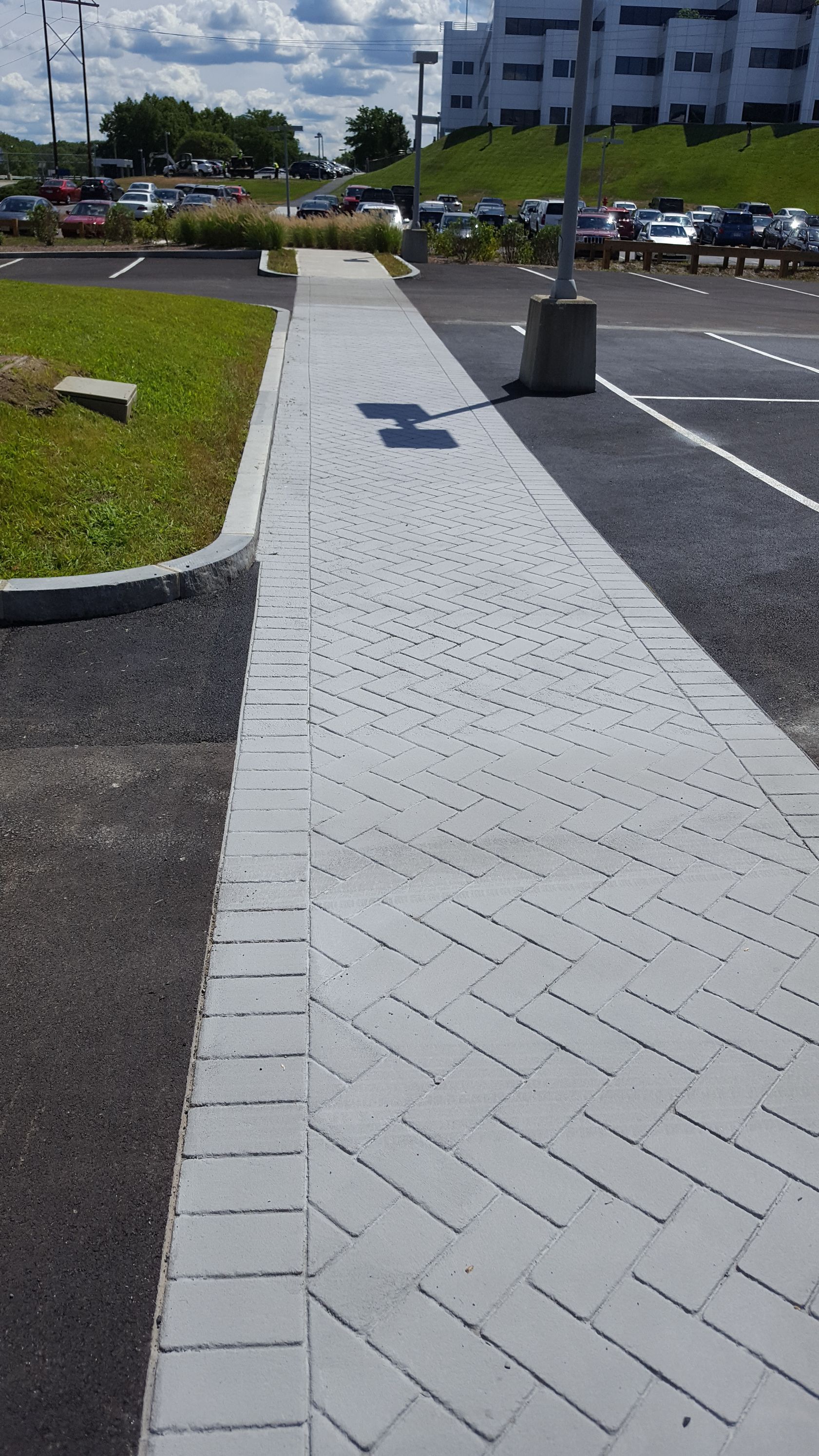A sidewalk leading to a parking lot with a building in the background.