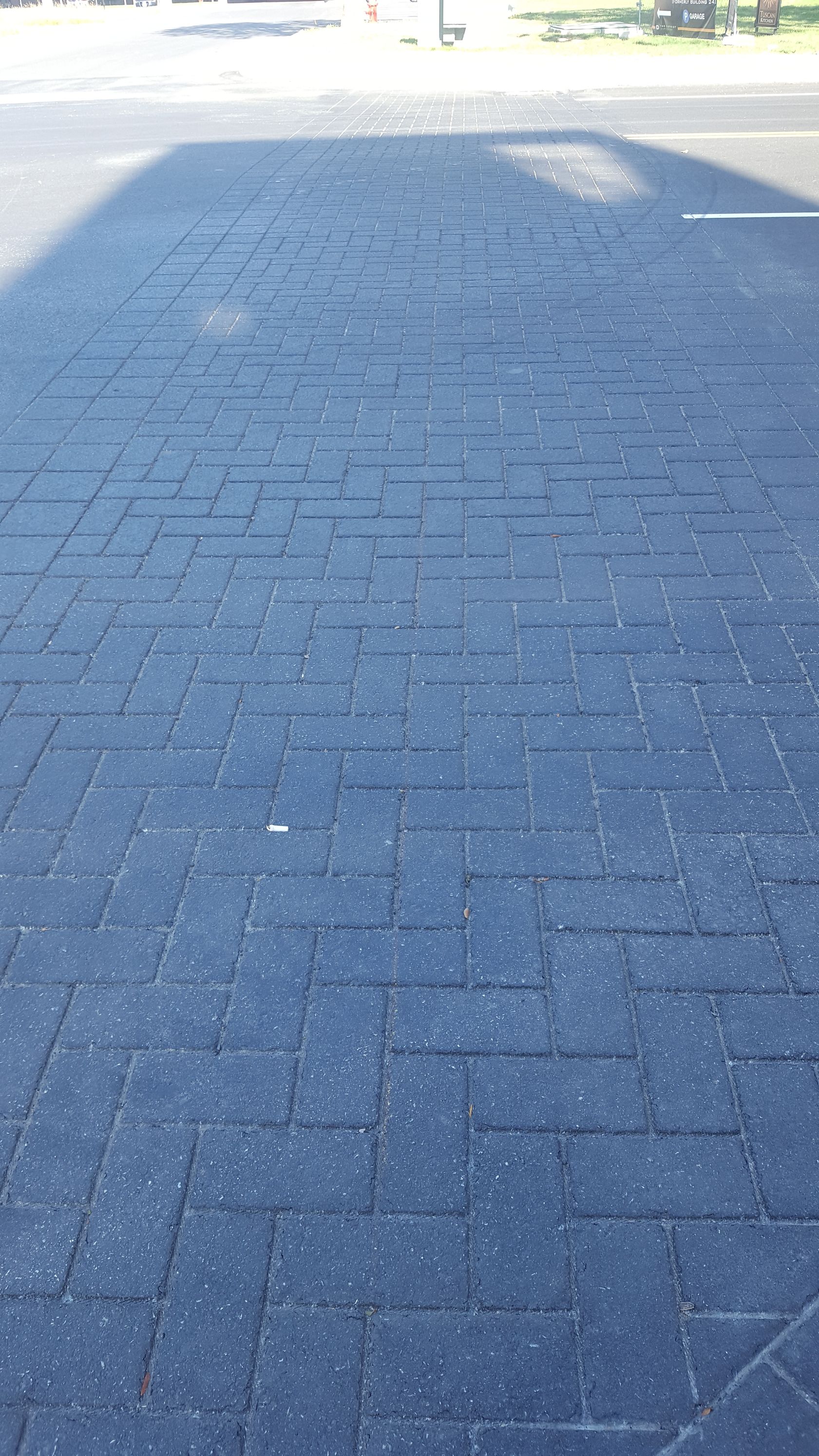 A shadow of a person is cast on a black brick walkway.