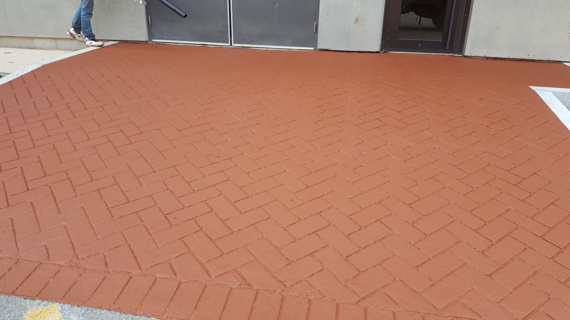 A person is walking on a red brick sidewalk in front of a building.