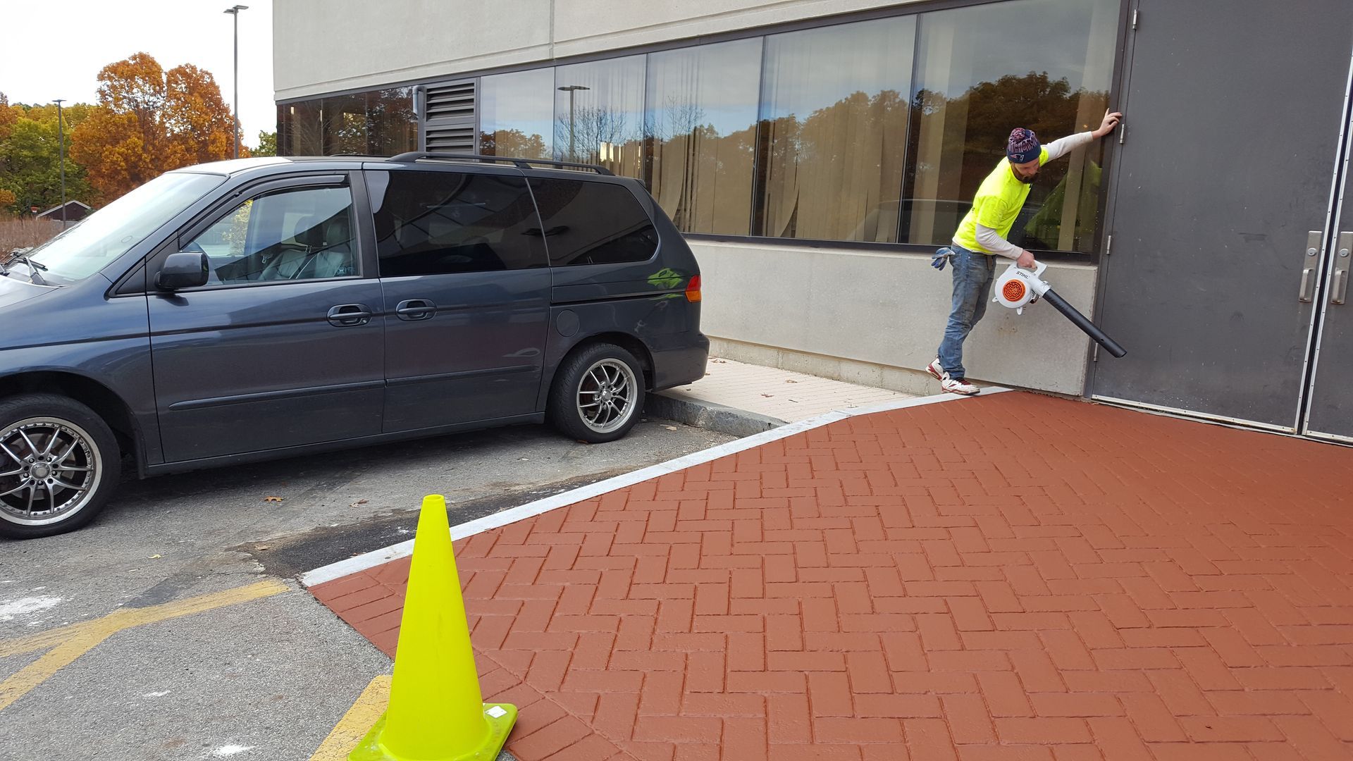 A man is cleaning a building with a blower in a parking lot.