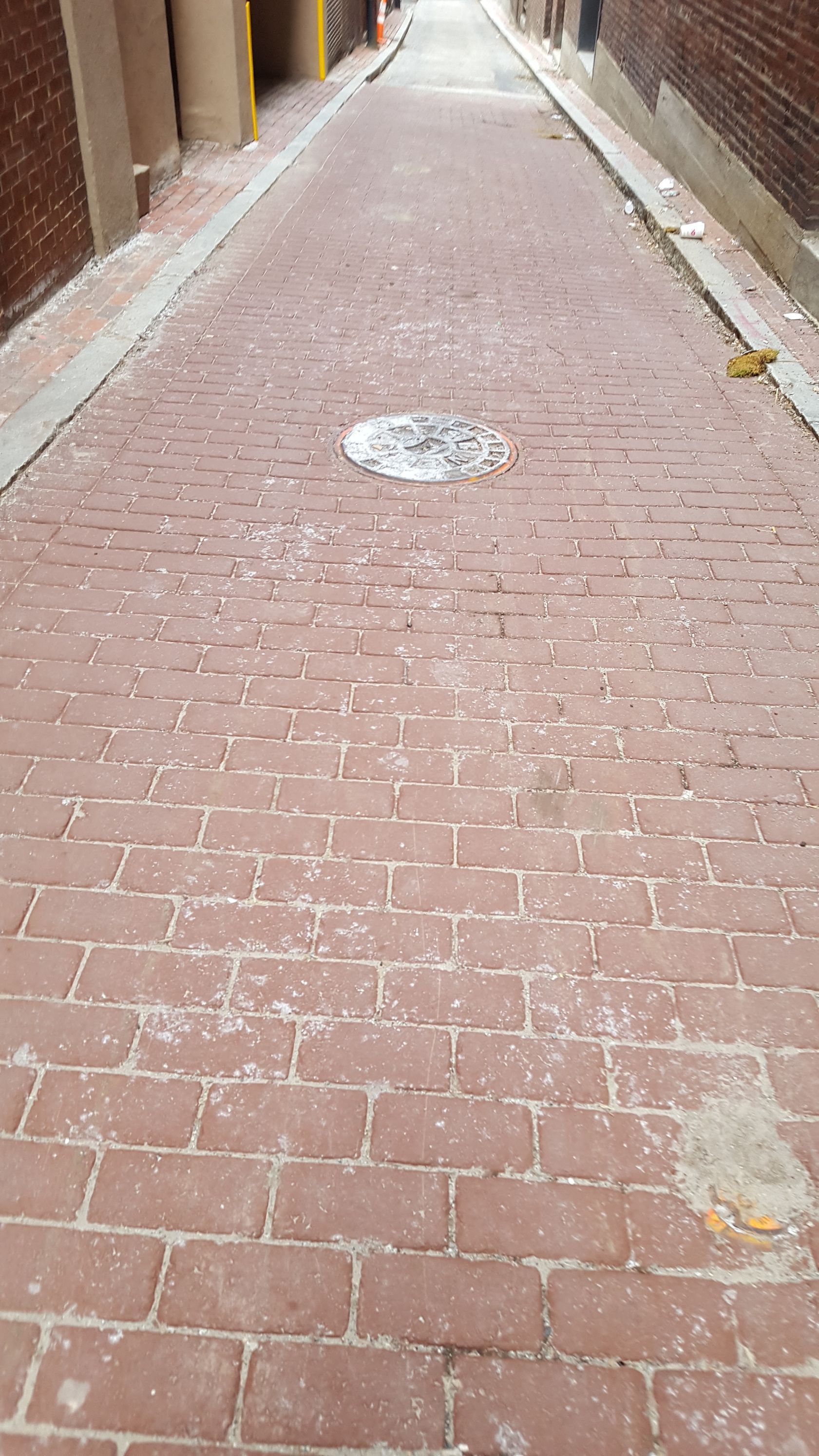 A narrow brick alleyway with a manhole cover in the middle.
