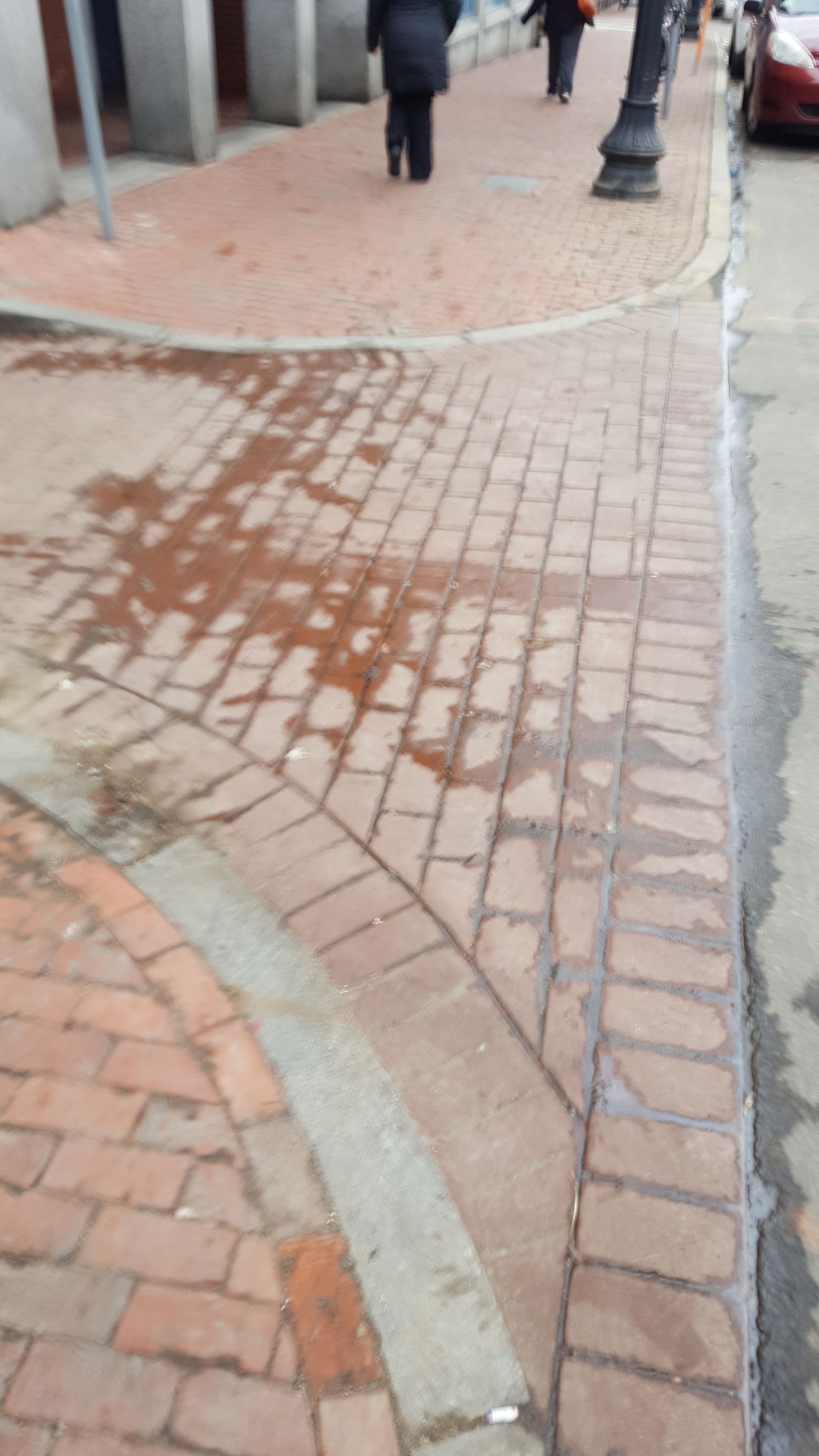 A red car is parked on the side of a brick sidewalk