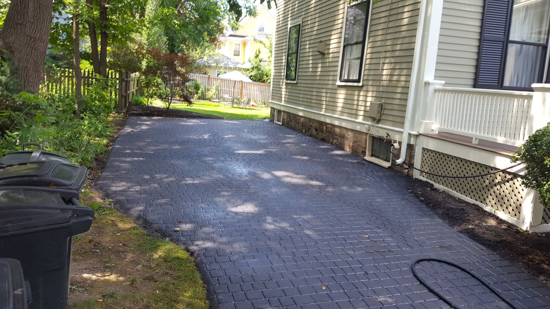 A brick driveway leading to a house with a trash can in the foreground.