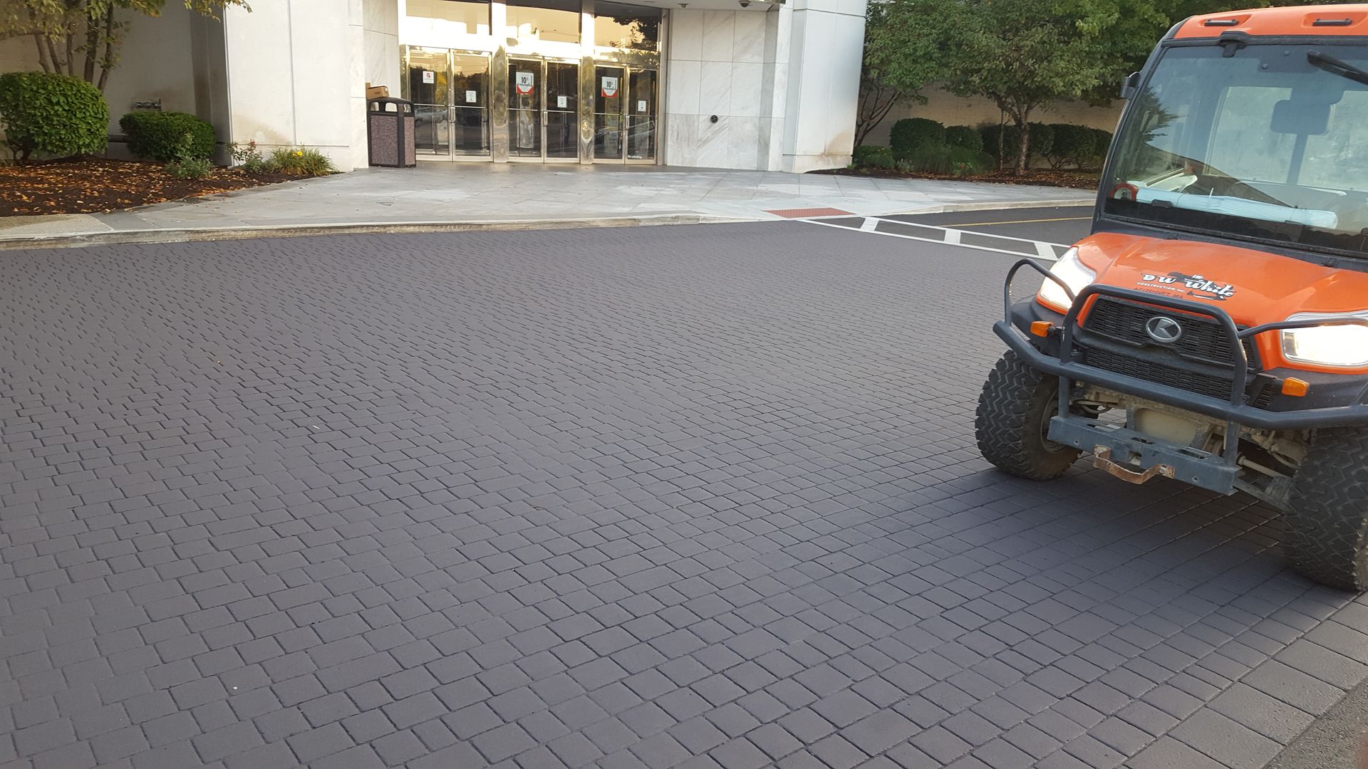 An orange vehicle is parked on a brick driveway in front of a building.