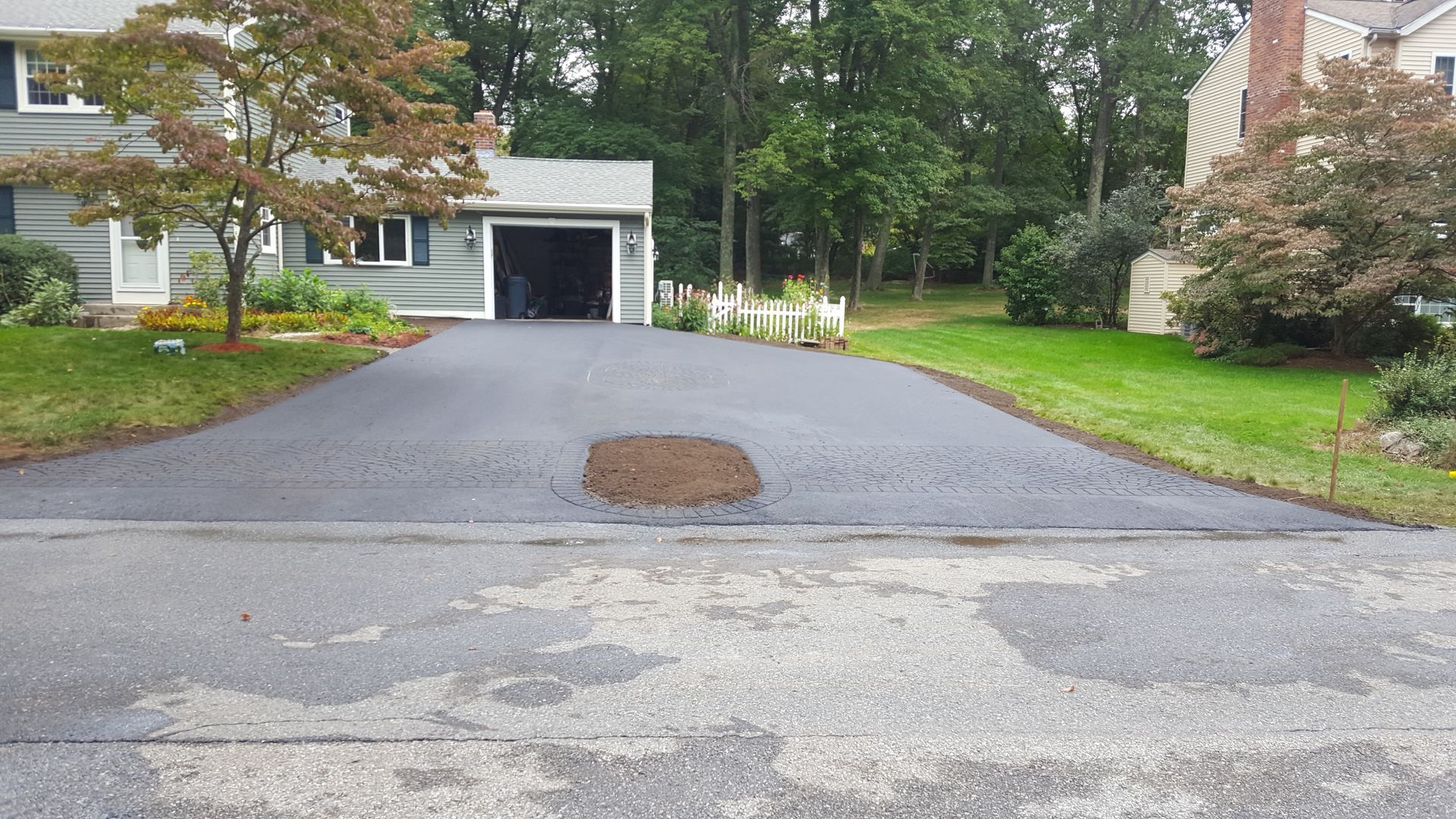A driveway leading to a house with a manhole cover in the middle of it.