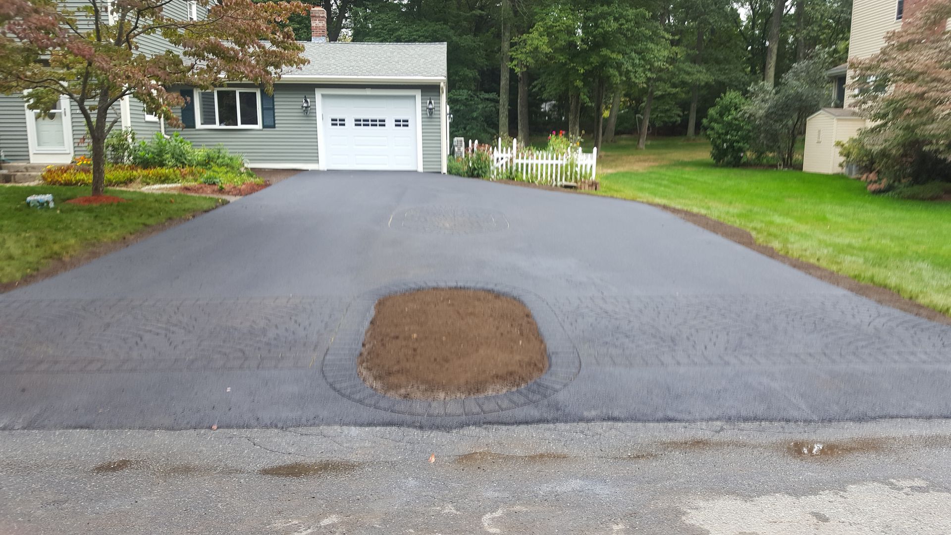 A driveway with a hole in it in front of a house.