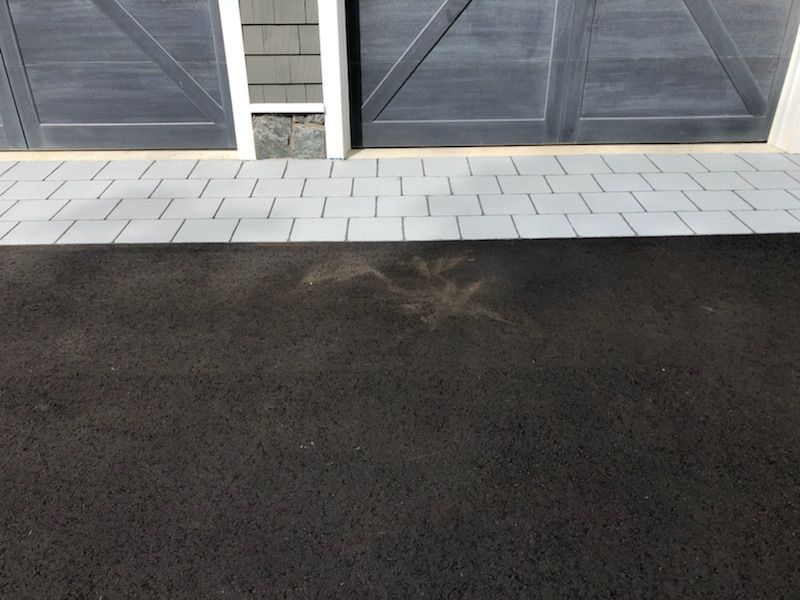 A black asphalt driveway next to a garage door
